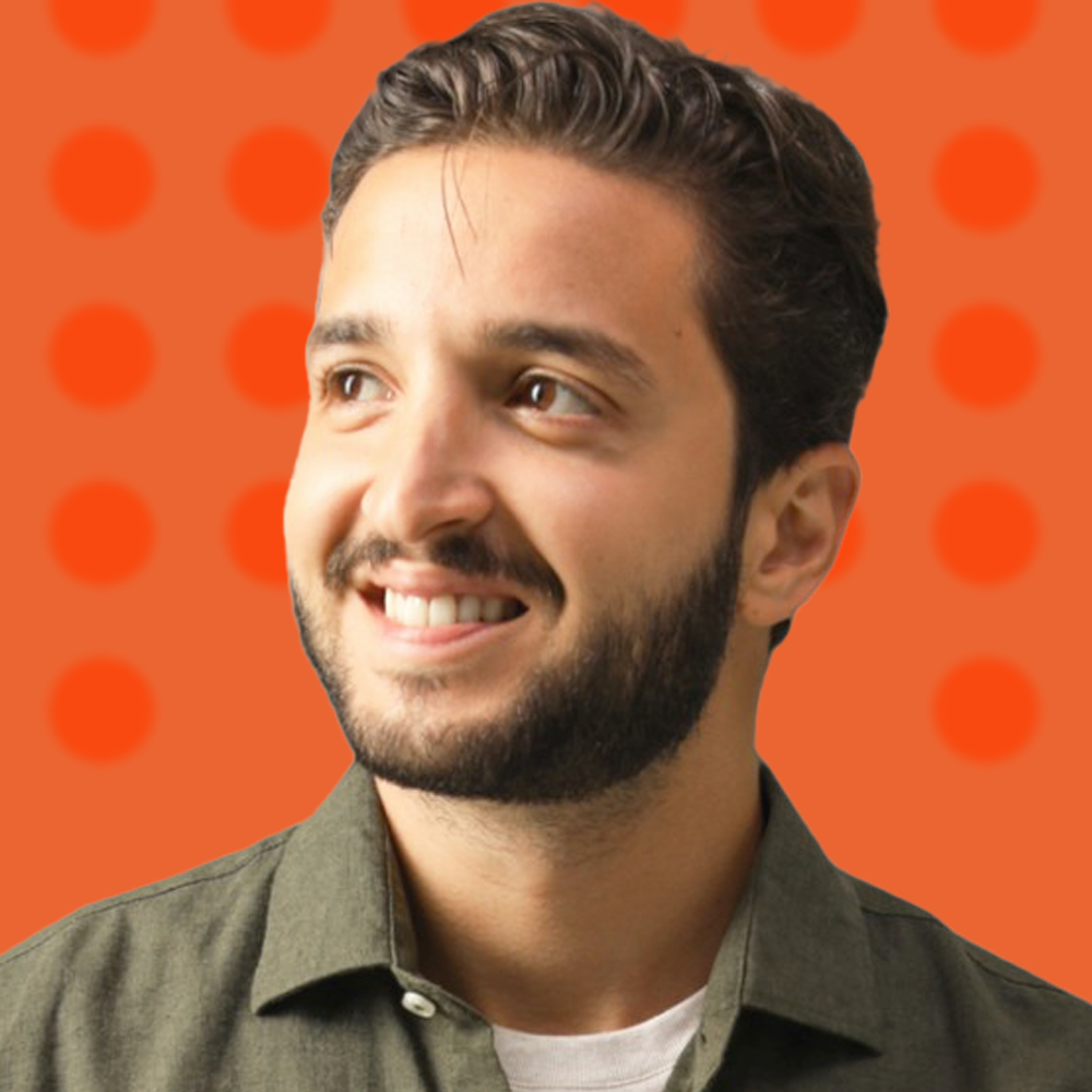 Portrait d'un homme souriant avec une chemise verte sur un fond orange à motifs de cercles.