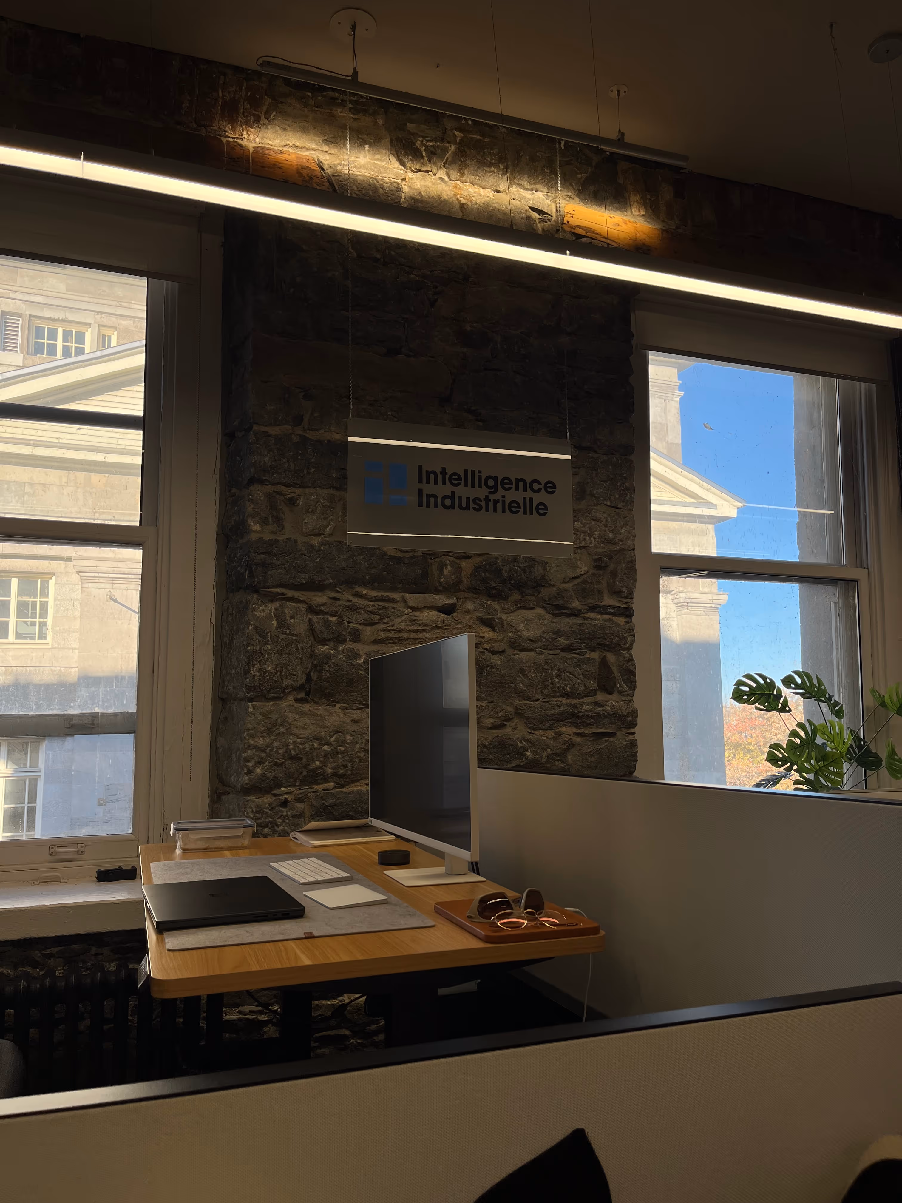 Modern Industrial Intelligence workspace in the Old Port of Montreal, with ergonomic workstation, large screen and logo on a stone wall, illustrating a warm technological environment.
