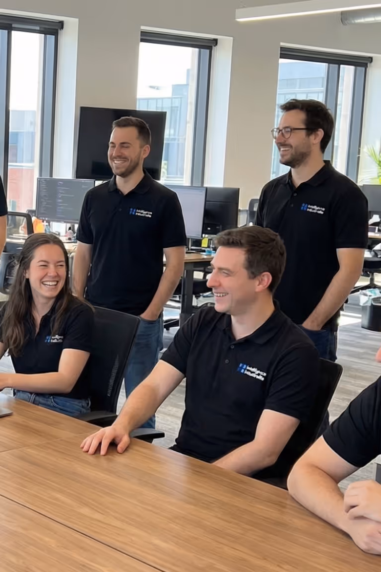 Team in the office in an informal meeting: colleagues in black polo shirts smiling around a table, collaborative and friendly atmosphere.