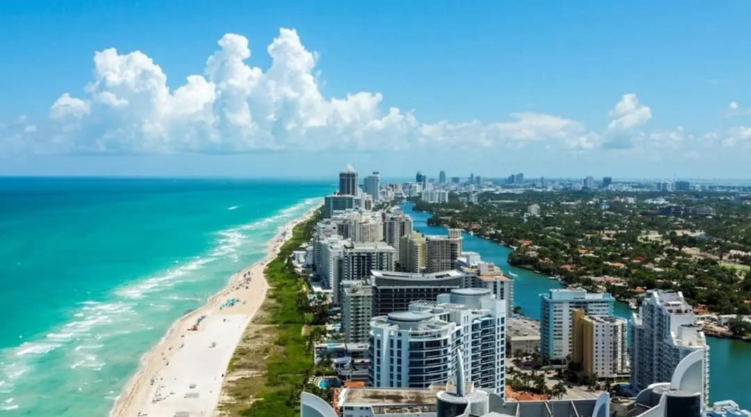 Florida coastal cityscape showing Miami Beach skyline, oceanfront condominiums, and the Atlantic Ocean from above.