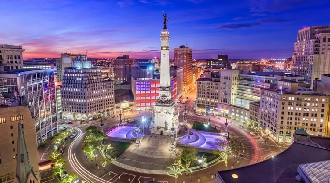 Indiana cityscape showing downtown Indianapolis with Monument Circle and surrounding buildings at twilight.