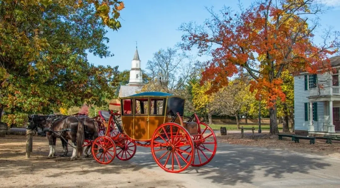 Historic Virginia street scene featuring a horse-drawn carriage, colonial architecture, and fall foliage.