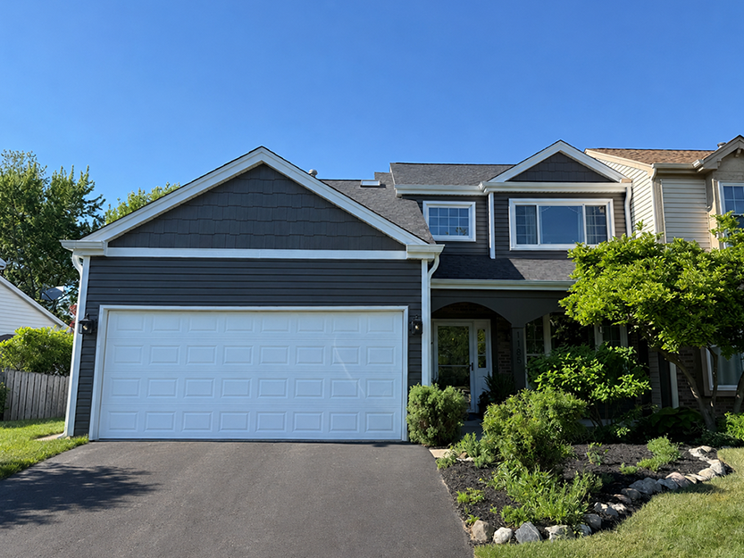 Two-story house with blue siding, white garage door, and landscaped front yard with shrubs and small tree.