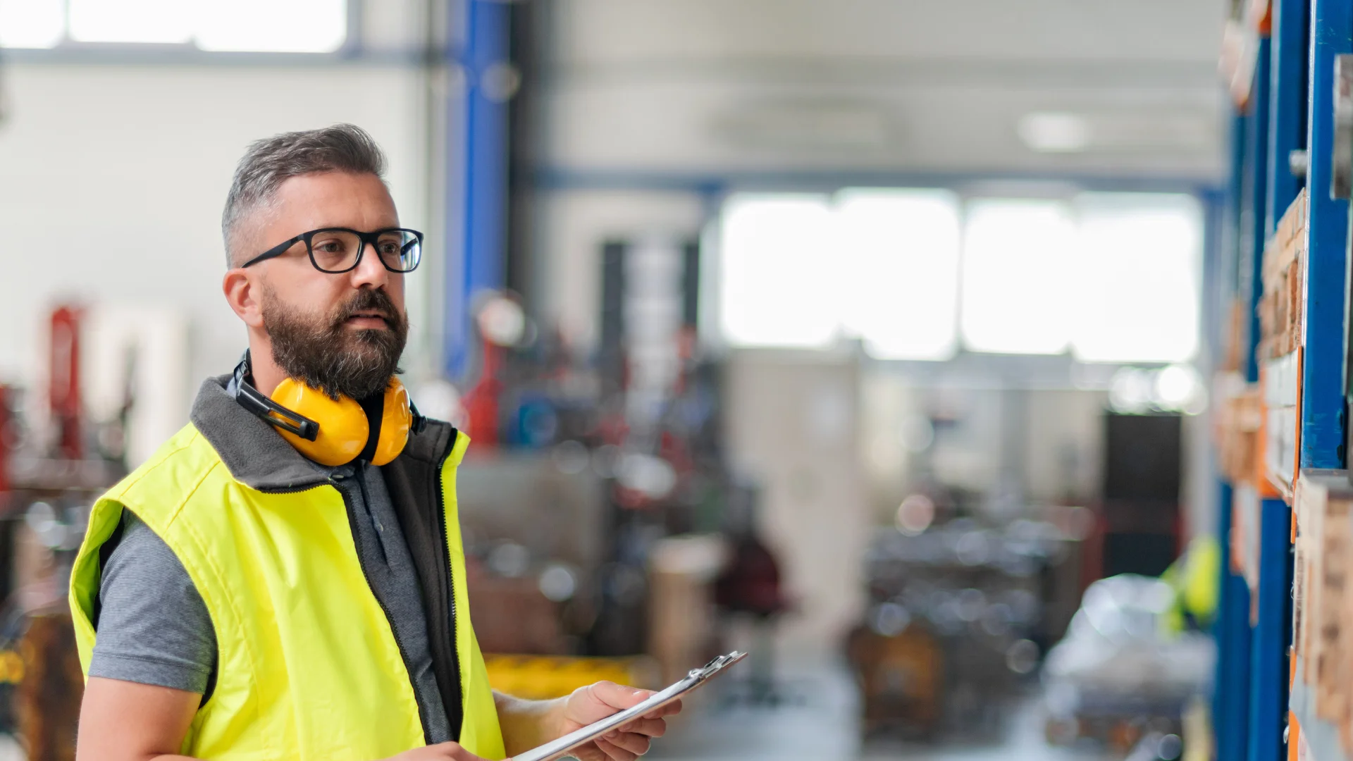 A warehouse worker wearing high-visibility gear and ear protection in an industrial setting, illustrating the environment where smart glasses and Frontline Intelligence provide real-time, hands-free support to prevent execution errors.