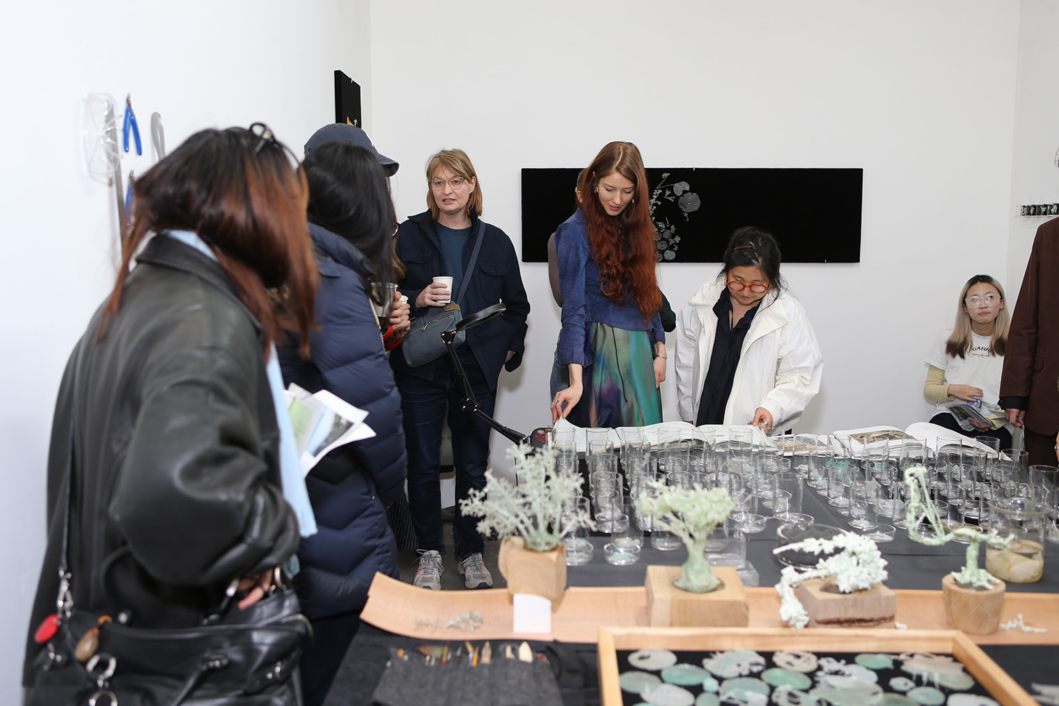 Sunset Park Open Studios 2026: visitors in winter coats gather around a table of small potted plant sculptures and ceramic pieces in a studio.