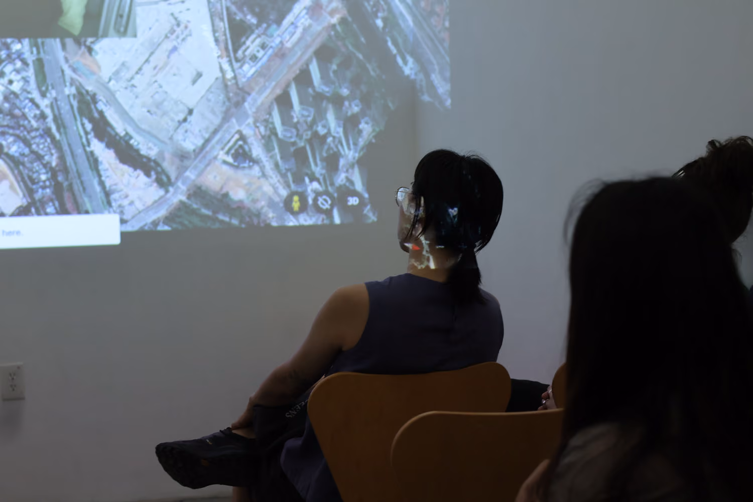 NARS Spring Open Studios 2026: two seated visitors watch a projected aerial map view of a waterfront area on a wall.