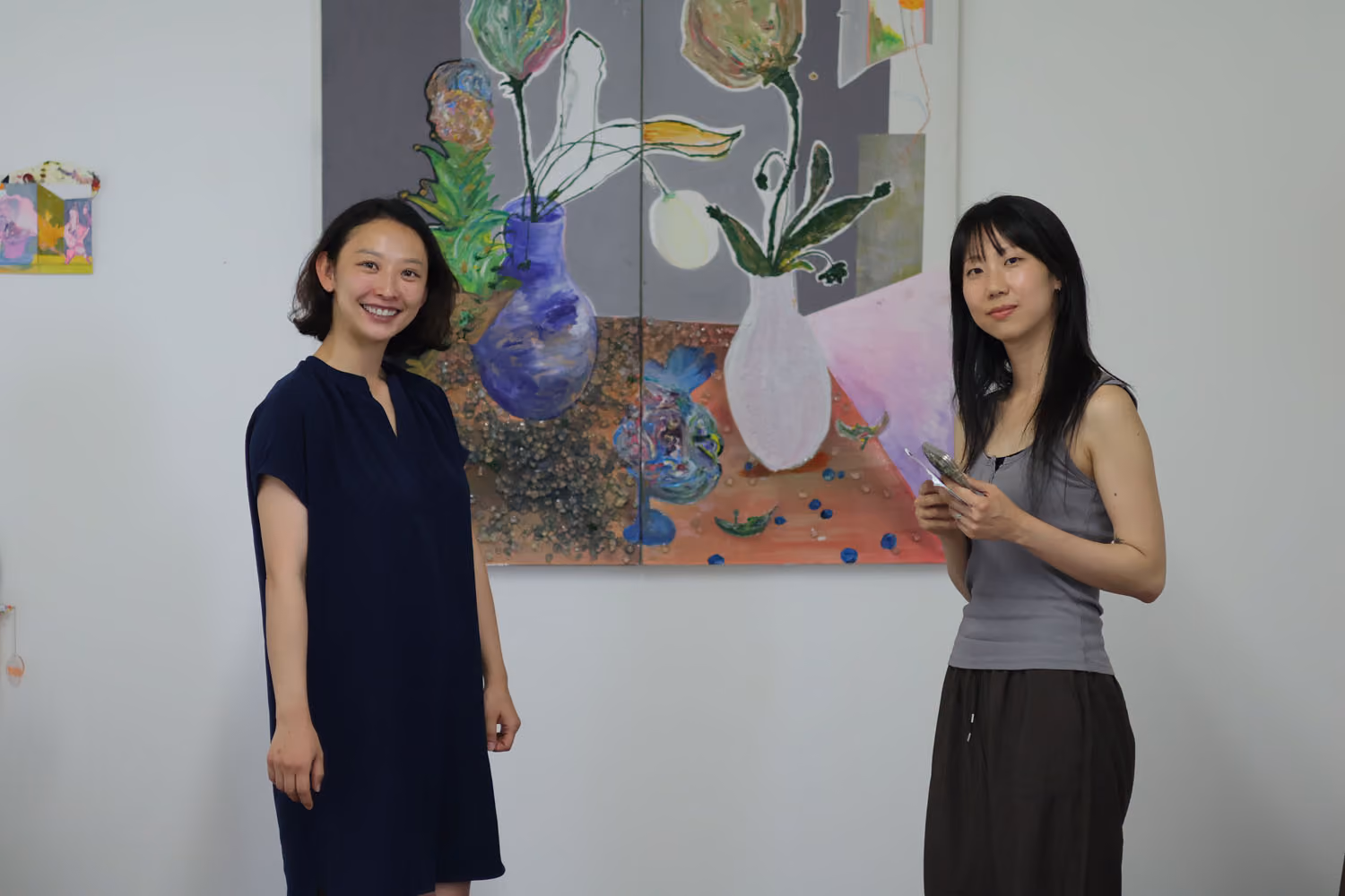 NARS Spring Open Studios 2026: two smiling women stand in front of a painting of flowers in vases on a gray and orange ground.