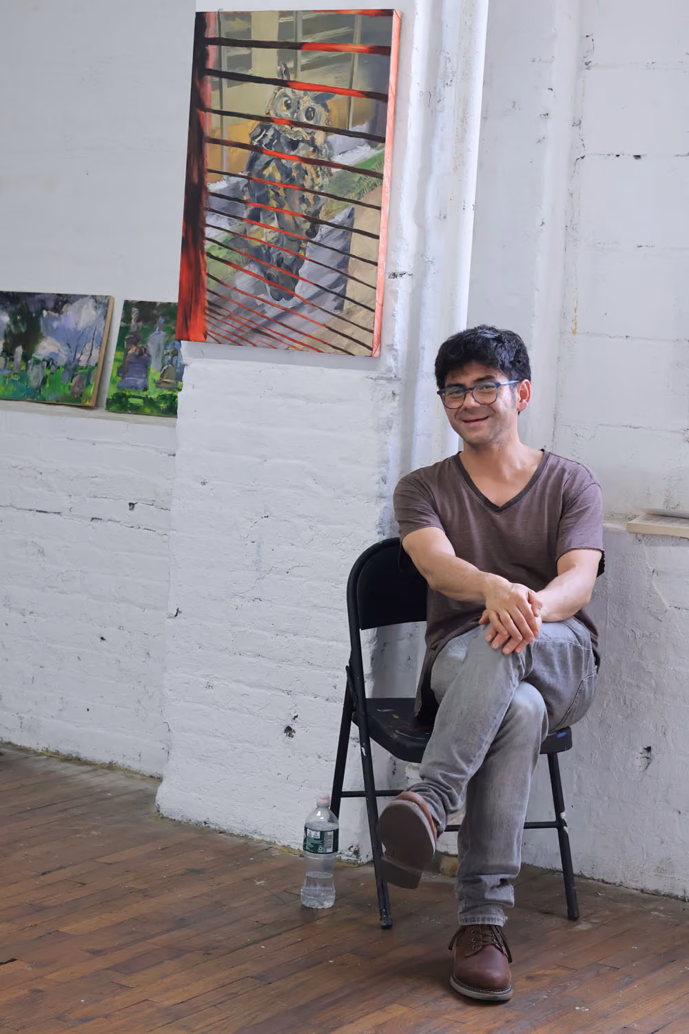 NARS Spring Open Studios 2026: a smiling man sits on a folding chair in a brick-walled studio beneath a framed painting.