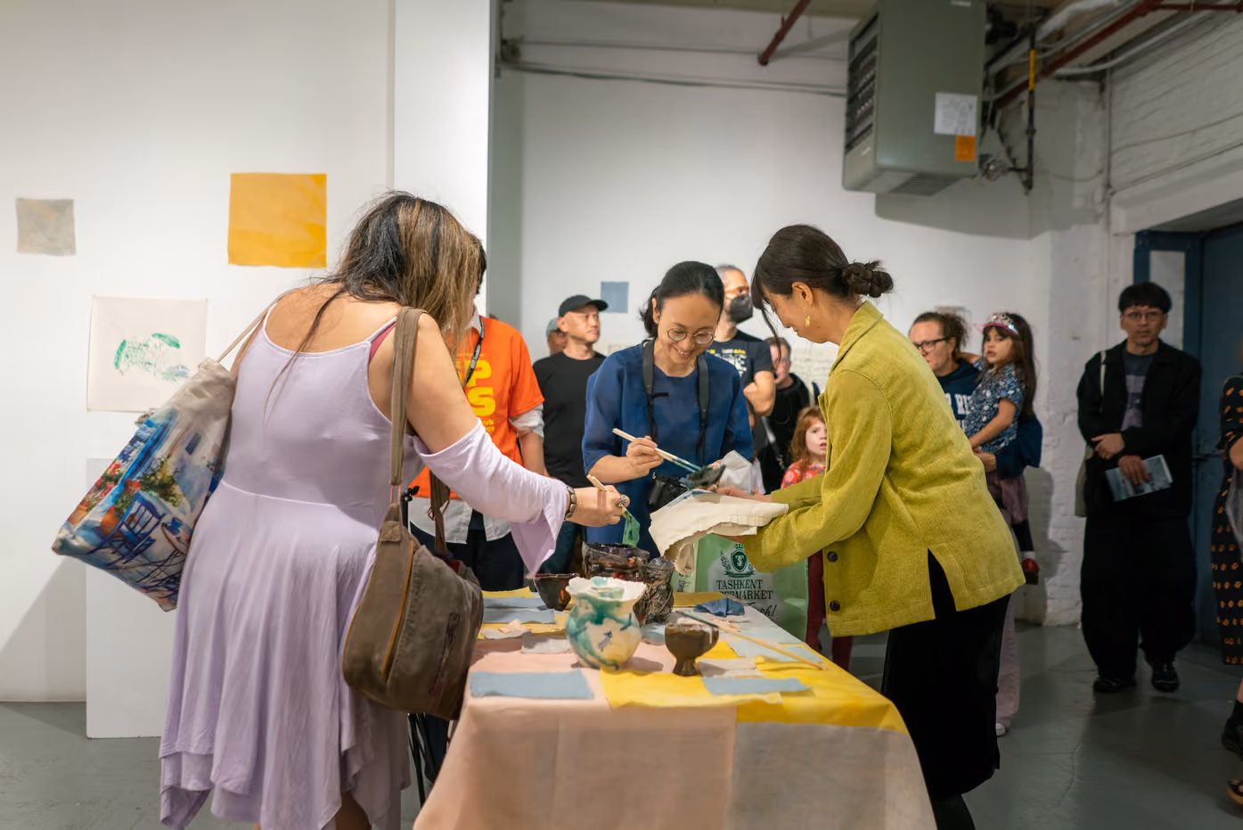 Photographed by Wei Chao. Visitors gathered closely around an interactive art table with ceramic vessels, dipping tools, and fabric swatches.