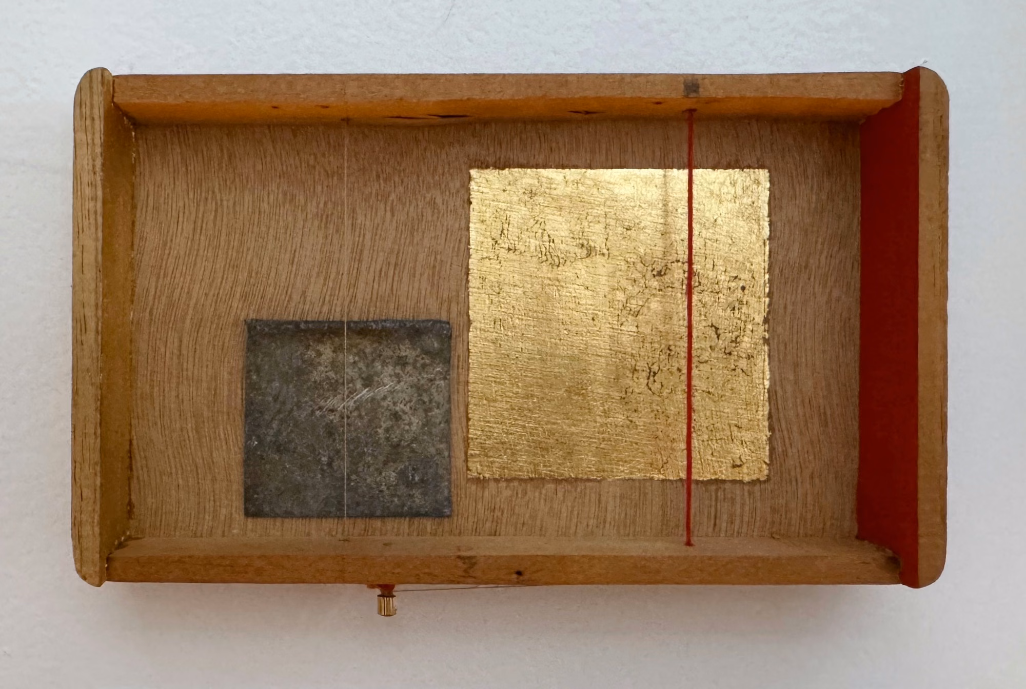 Nicholas Rynearson, Untitled (Te Amo 1), 2025: wooden cigar box on a wall holding a square of gold leaf, a dark metal square, and a red thread.