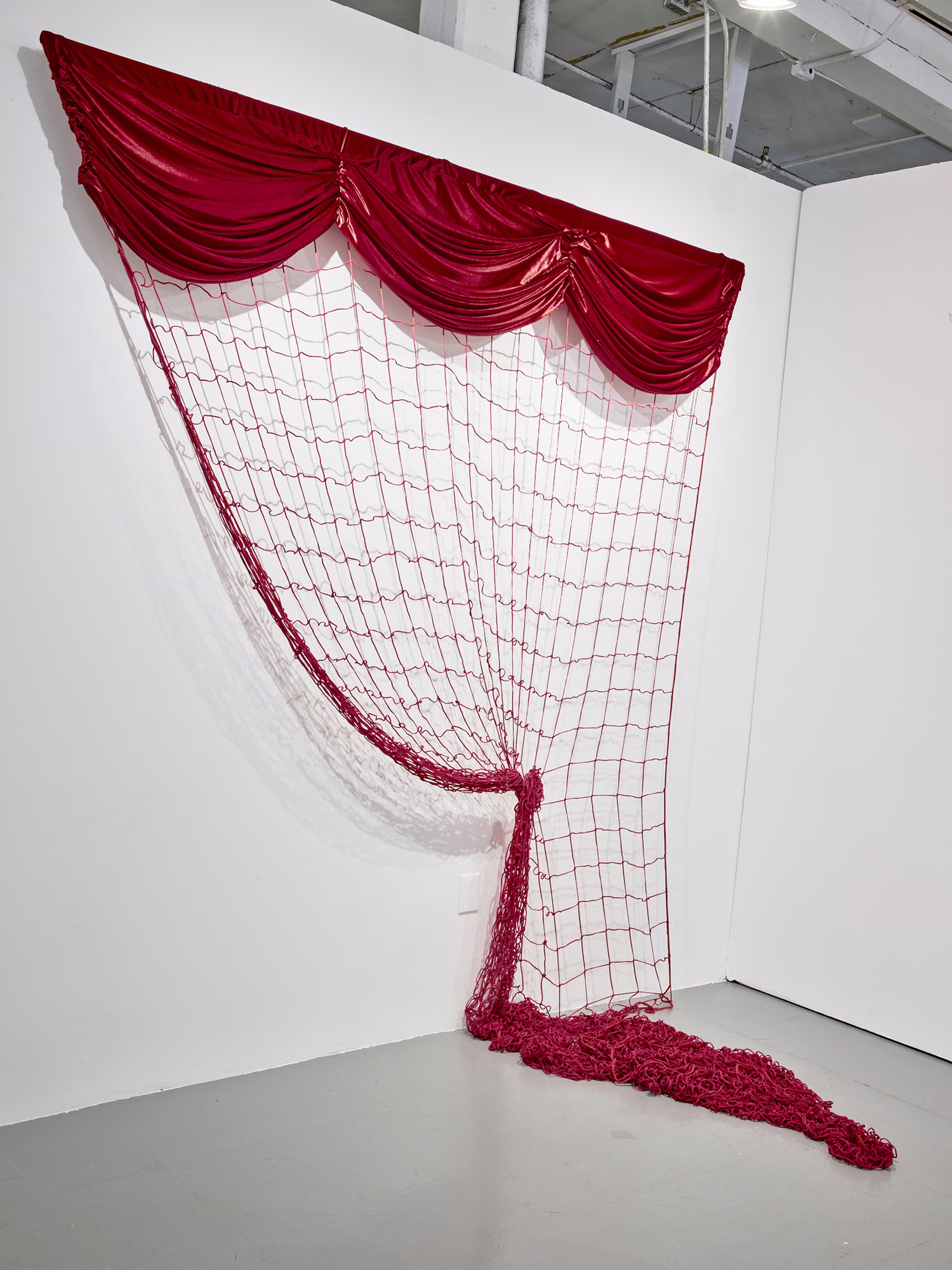 Work in Toward a Sentence: a red theater-style valance and red netting hang in a gallery corner, with knotted red rope pooled on the floor.