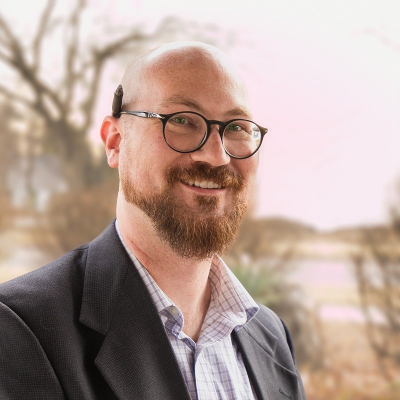 Dr. Kyle A. Hammonds standing outside with trees and sunlight in the background