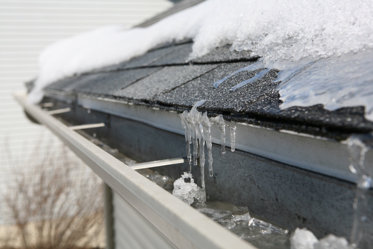 standard frozen roof with ice and snow over asphalt shingles right before entering the gutter.