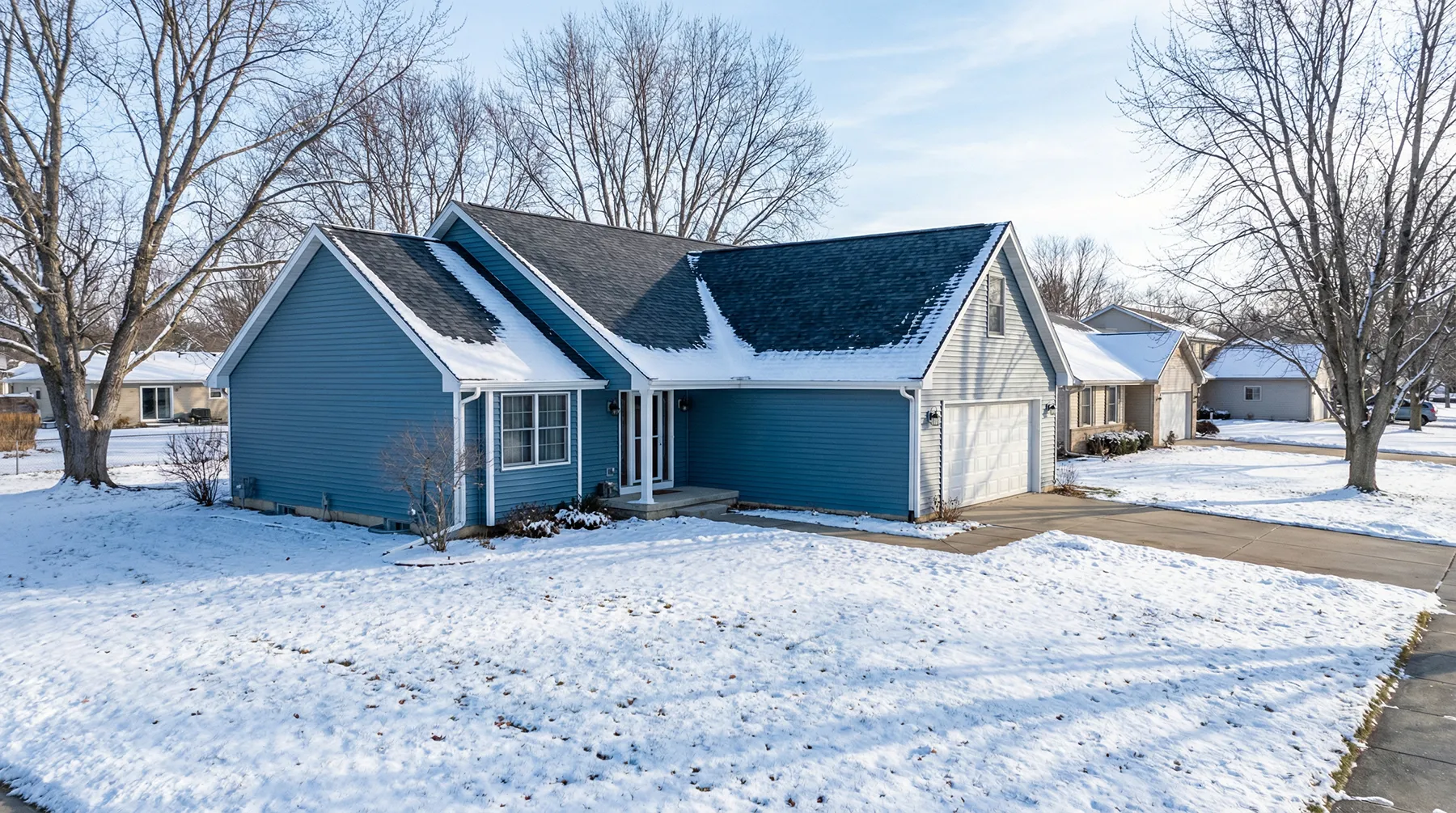 Blue suburban single-family home with attached garage, snow-covered roof and yard in a winter neighborhood.