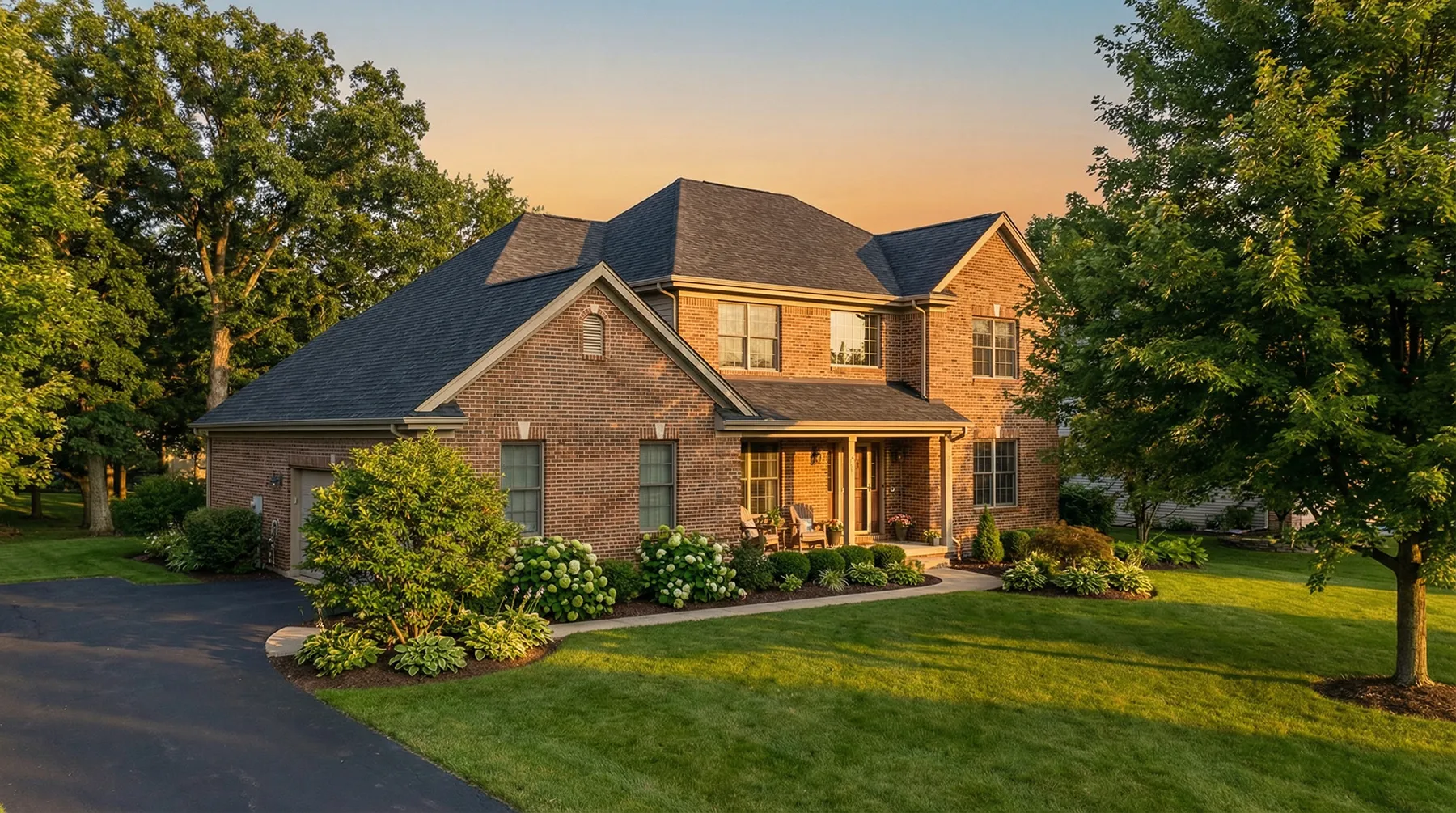 Two-story brick suburban home with attached garage, covered porch, and well-maintained landscaping at sunset.