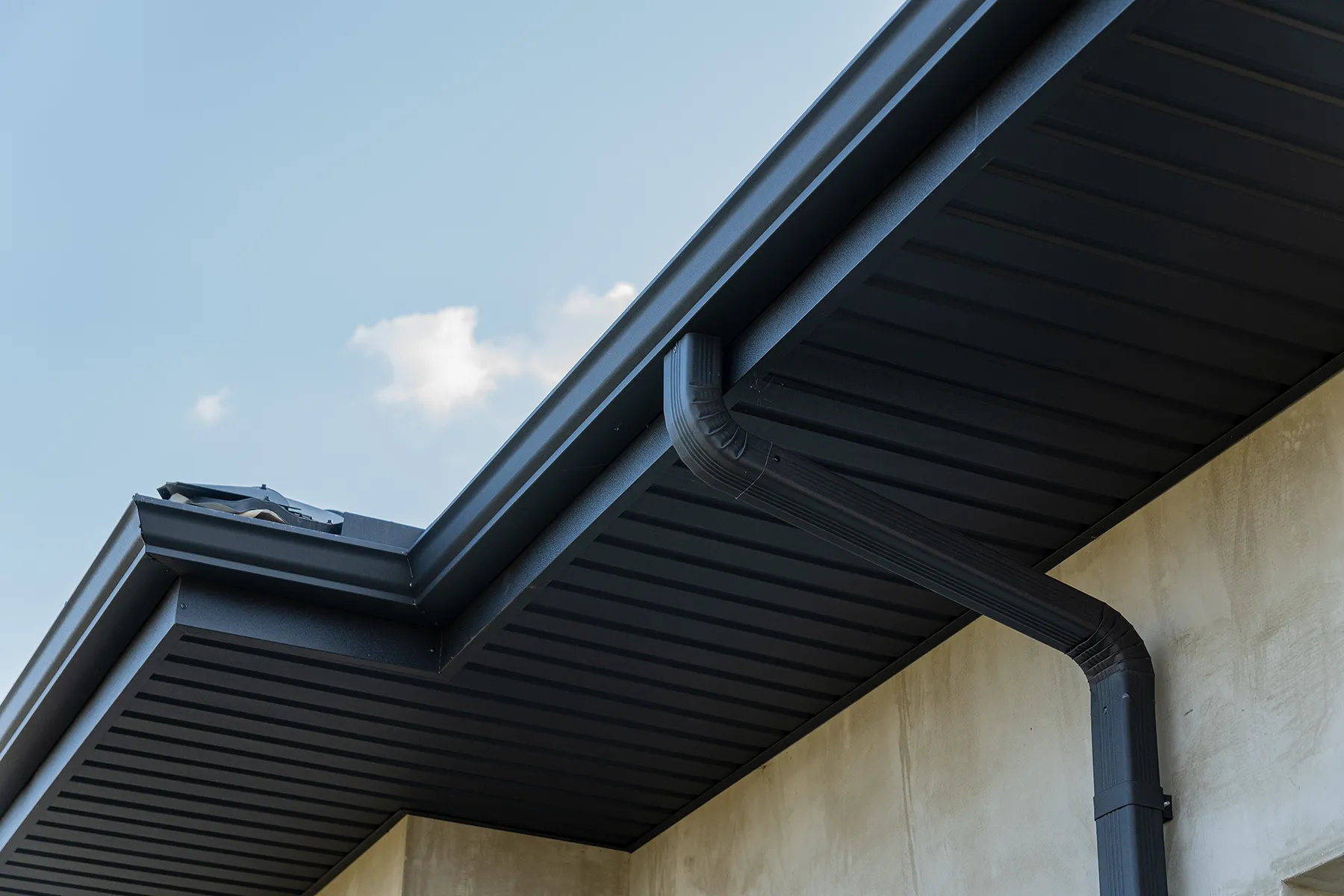 Seamless black metal soffit, fascia, and gutter system with downspout on house exterior.