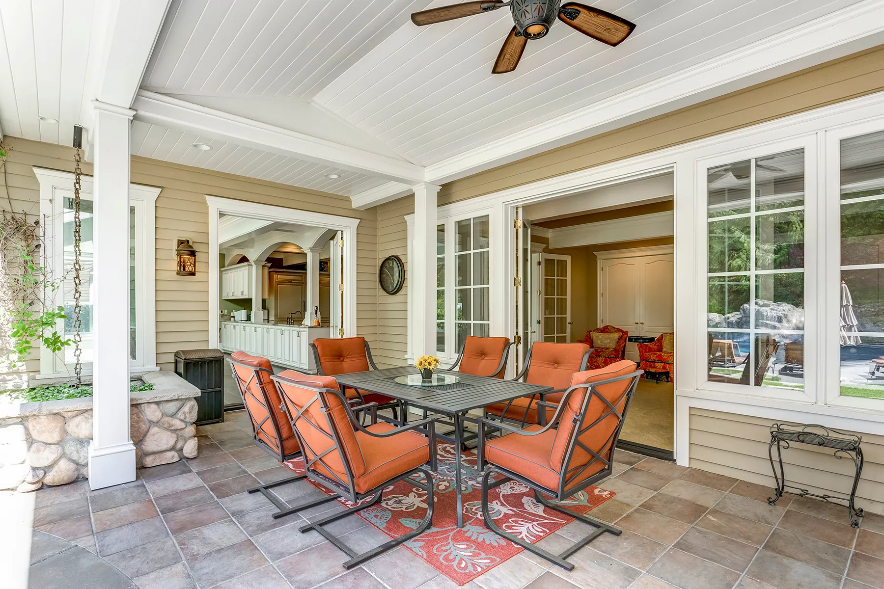Outdoor covered porch with ceiling fan, dining table and chairs on tiled floor, and vinyl siding exterior.