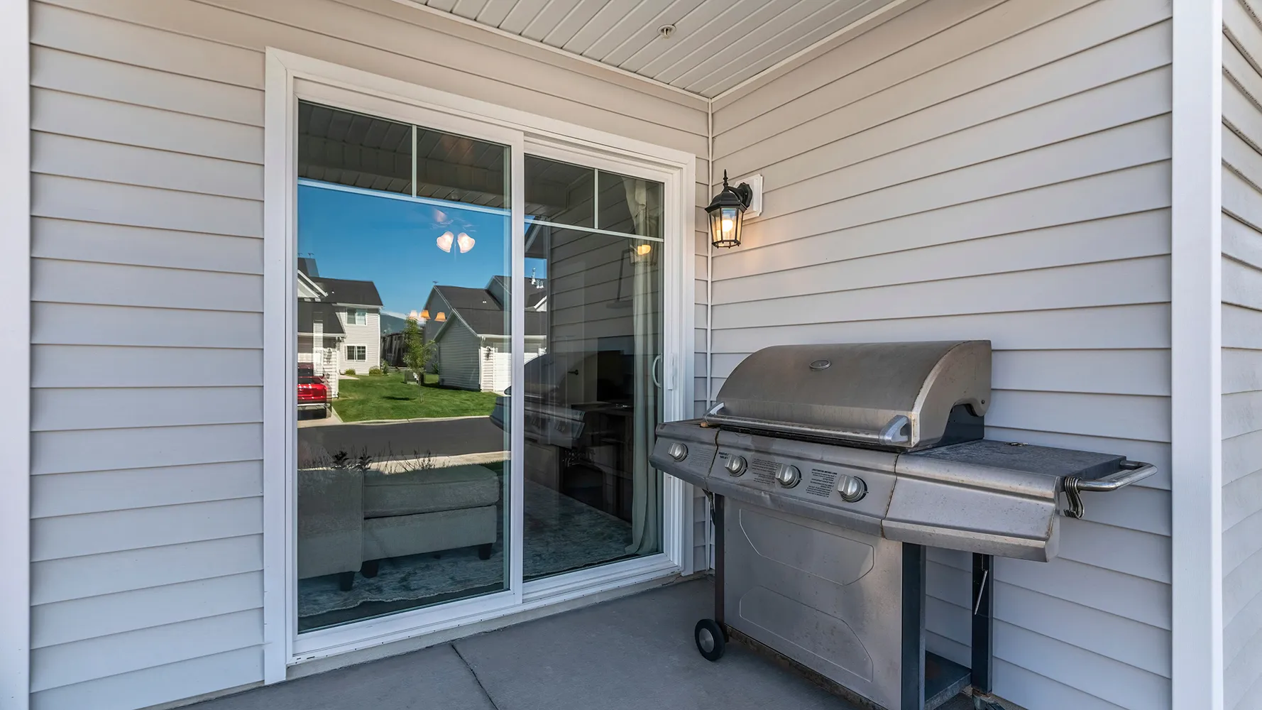 Covered patio with vinyl siding walls, sliding glass door, gas grill, and concrete floor.
