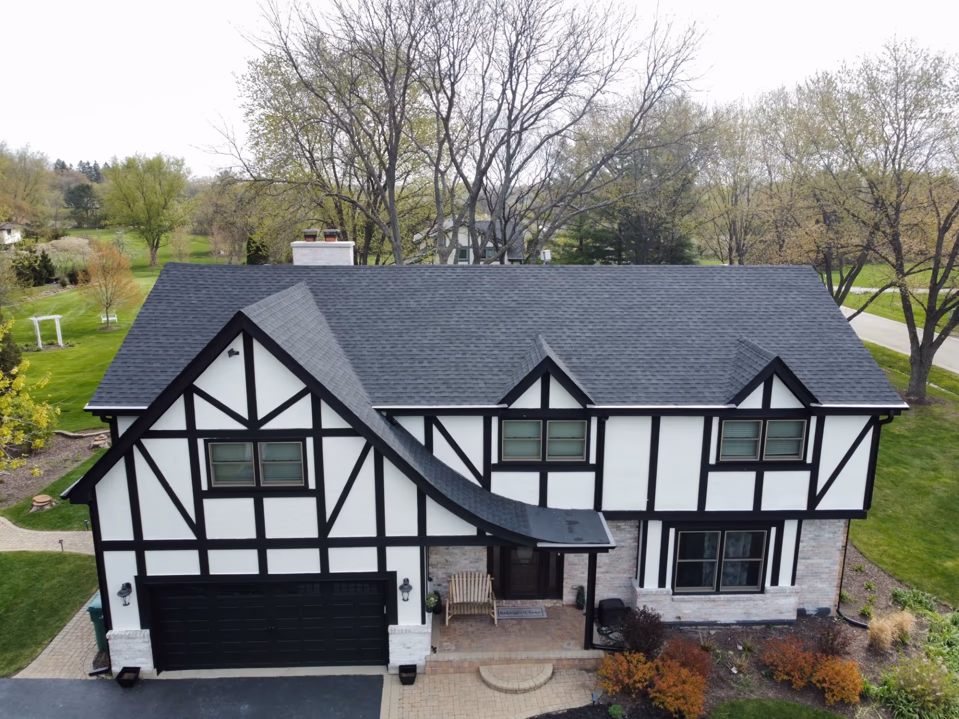 Aerial view of Tudor-style home with white stucco, black timbering, stone base, and newly installed dark asphalt shingle roof.