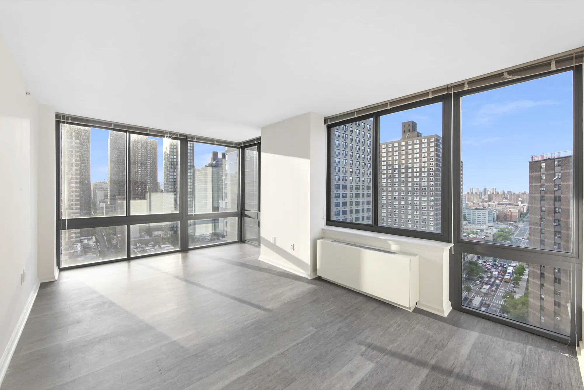 An empty apartment featuring large windows and polished hardwood floors, showcasing a bright and spacious interior.