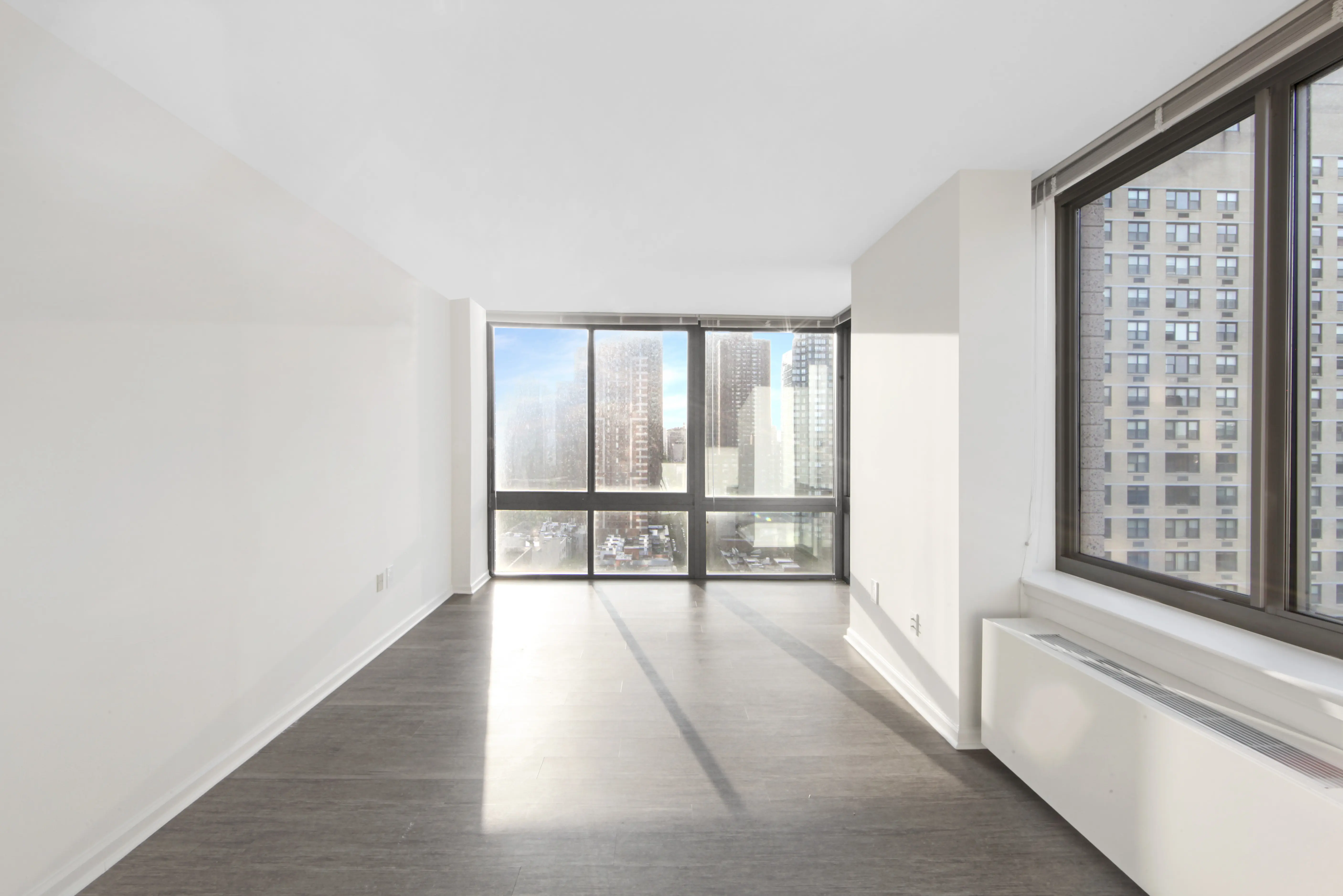 A spacious, empty room featuring hardwood floors and large windows allowing natural light to enter.
