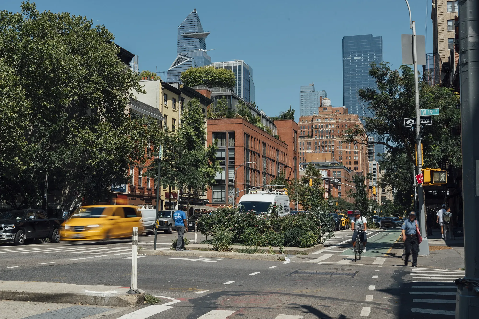 A city street scene with a yellow taxi and a man casually walking past shops and buildings.