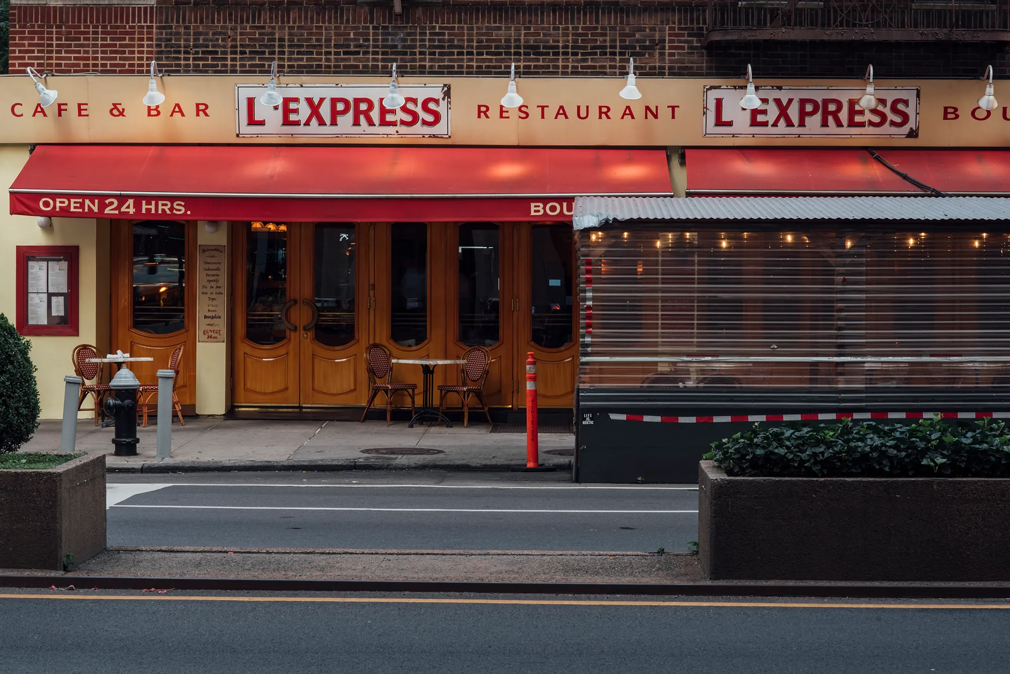 A vibrant red awning extends over a quaint cafe, providing shade and a welcoming atmosphere for patrons.