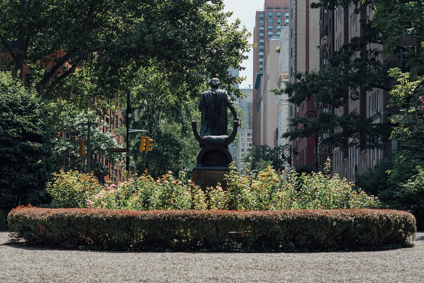 A statue of a man seated on a bench in a park, surrounded by greenery and pathways.