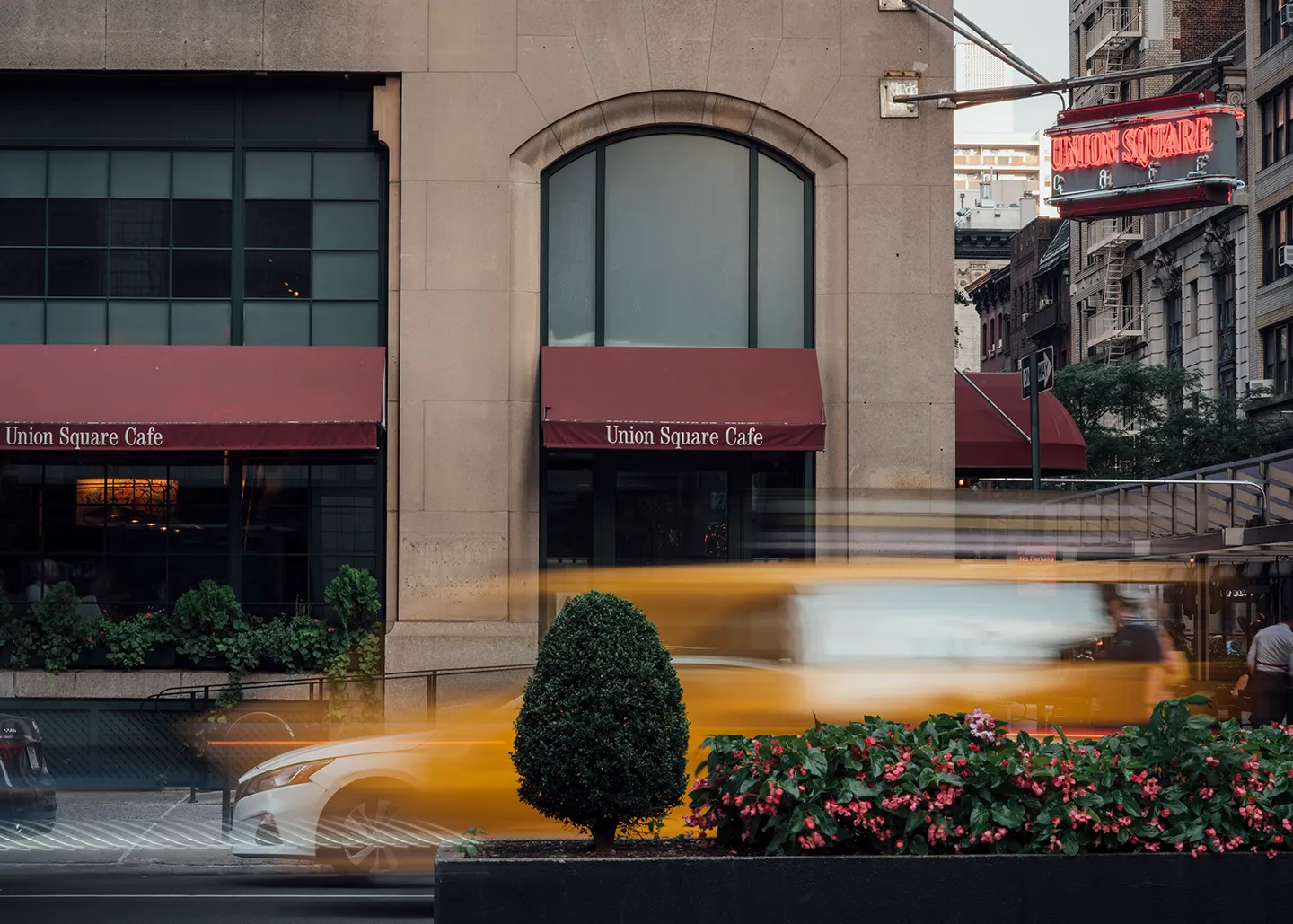 A yellow taxi cab drives down a busy street, surrounded by buildings and pedestrians.