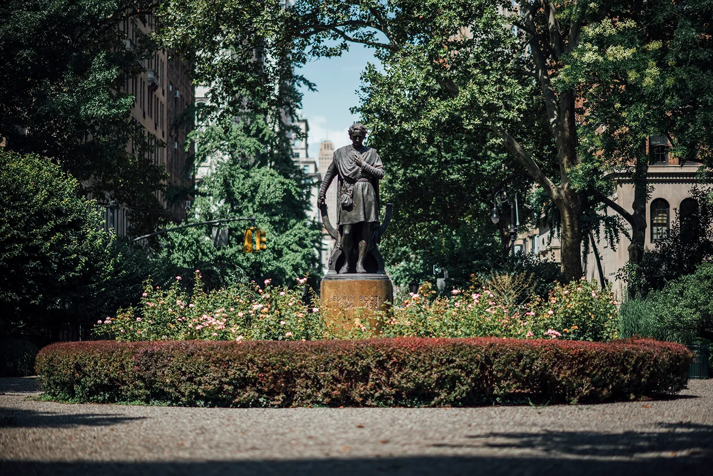 A statue of a man stands in a park, surrounded by lush green trees, creating a serene outdoor atmosphere.
