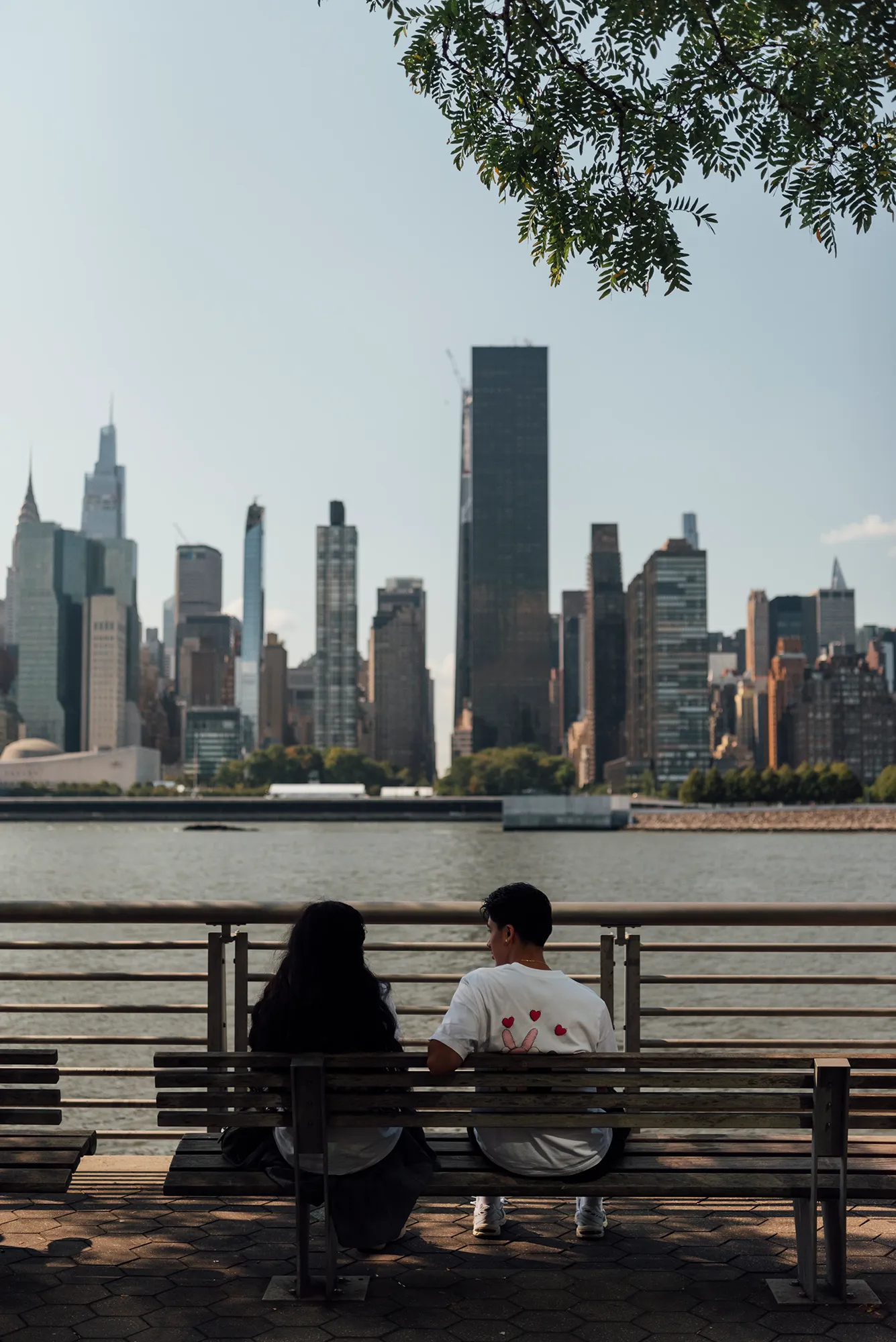 Two people sitting side by side on a wooden bench in a park, enjoying a conversation under a clear blue sky.