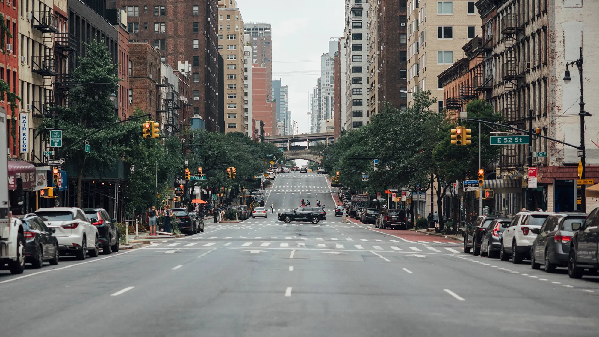 A bustling city street filled with cars, with tall buildings lining the background under a clear blue sky.