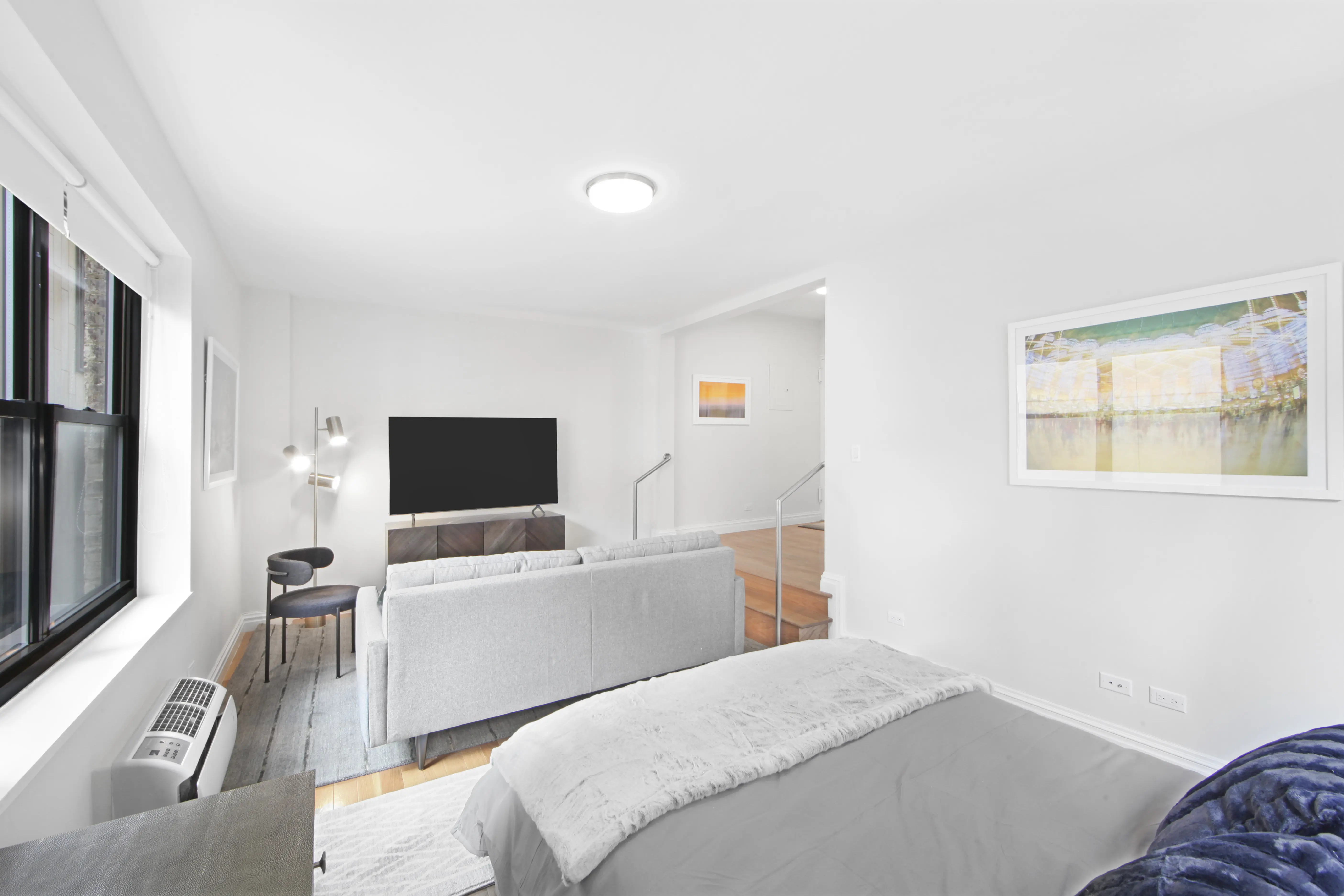 A bright, white bedroom with a neatly made bed, a cozy couch, and a television, creating a serene atmosphere.