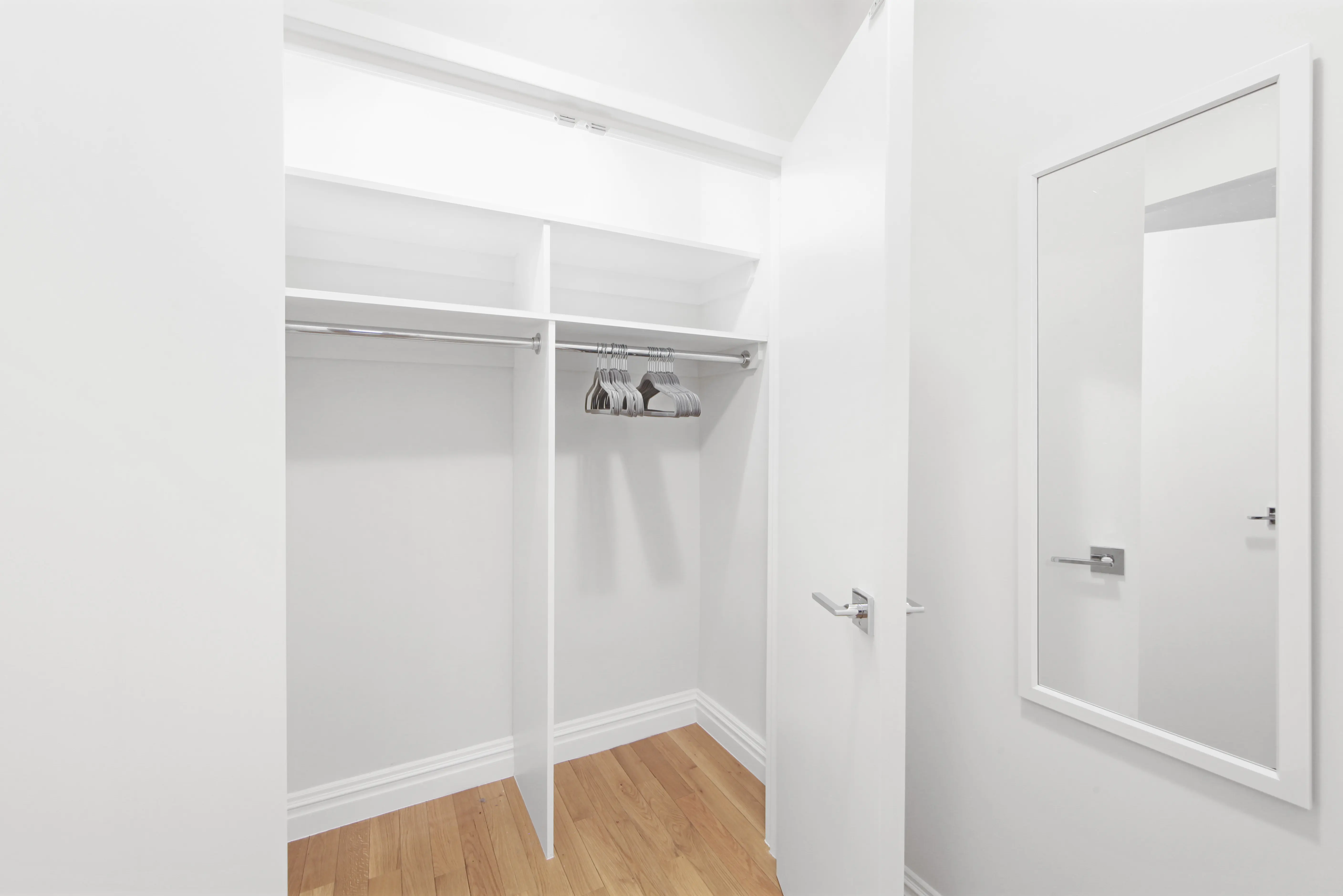 A white closet featuring a mirror and a shoe rack, showcasing organized footwear and reflective surface.