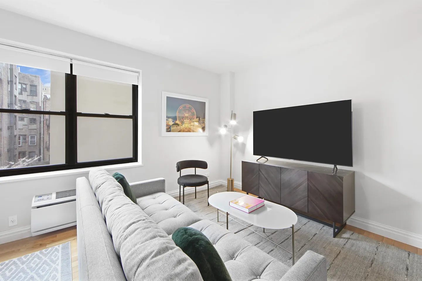 A cozy living room featuring a couch, chair, TV, and a window allowing natural light to enter.