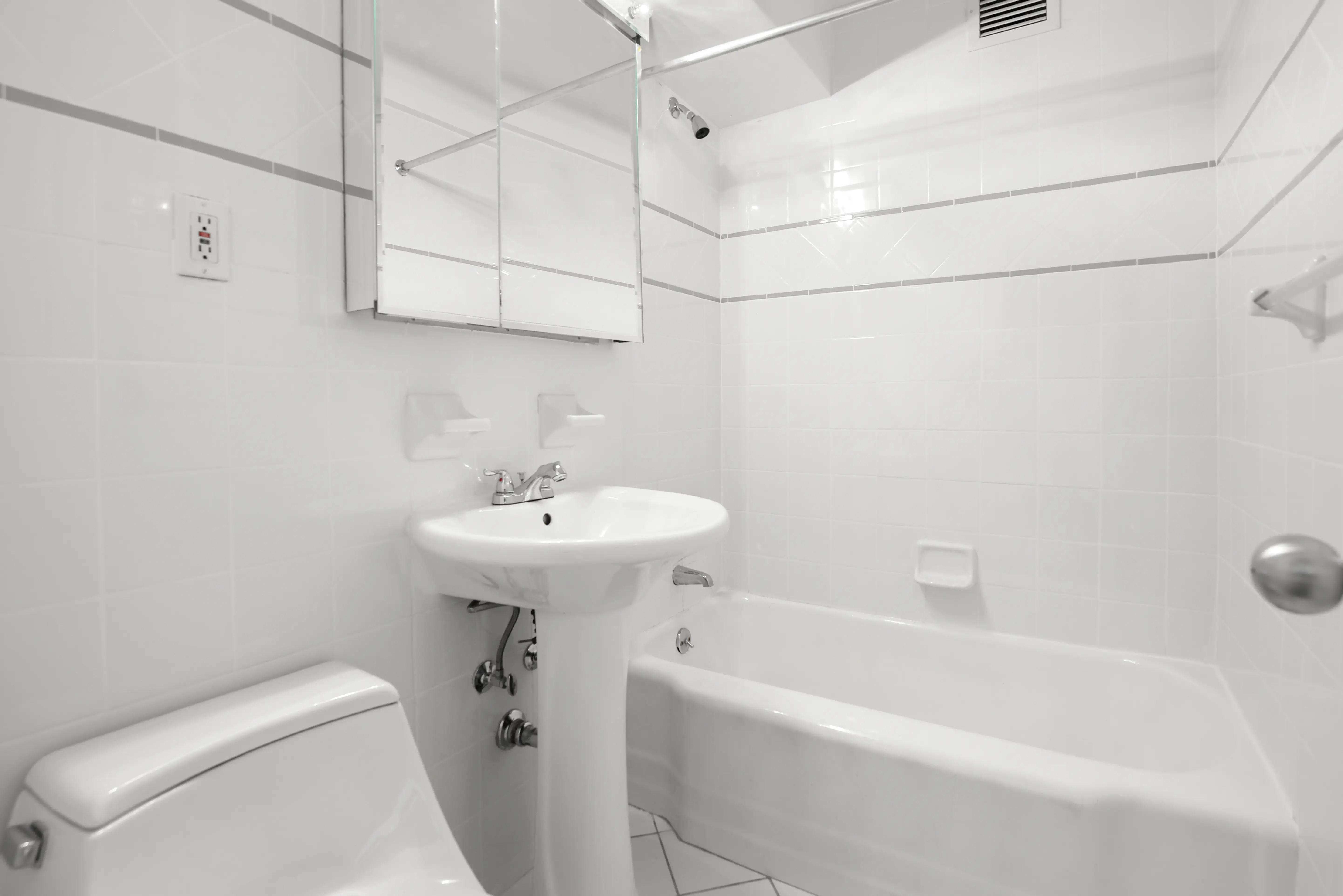A modern bathroom with white tiled walls, including a toilet, sink, and a bathtub.