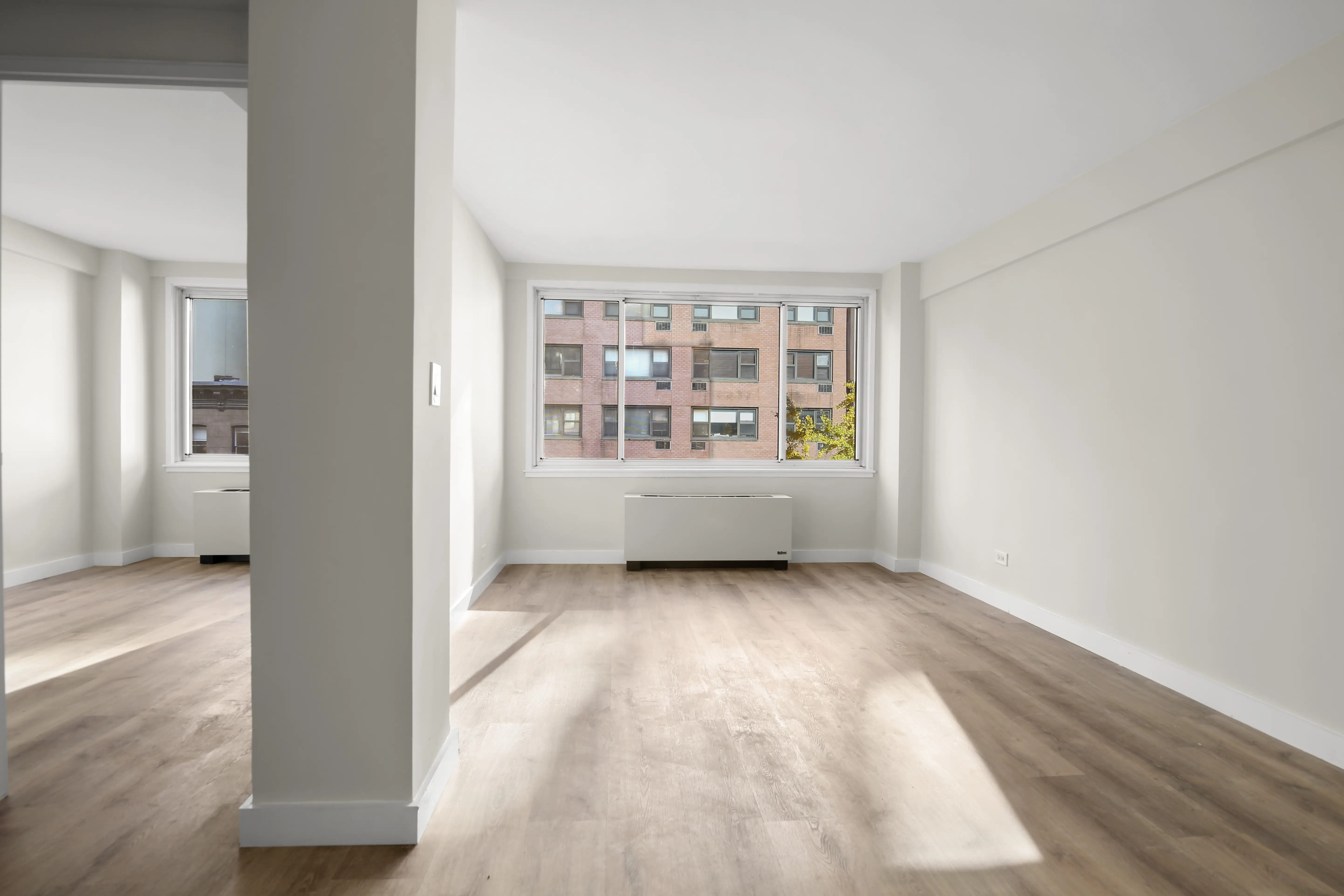 An empty apartment featuring hardwood floors and large windows allowing natural light to enter the space.
