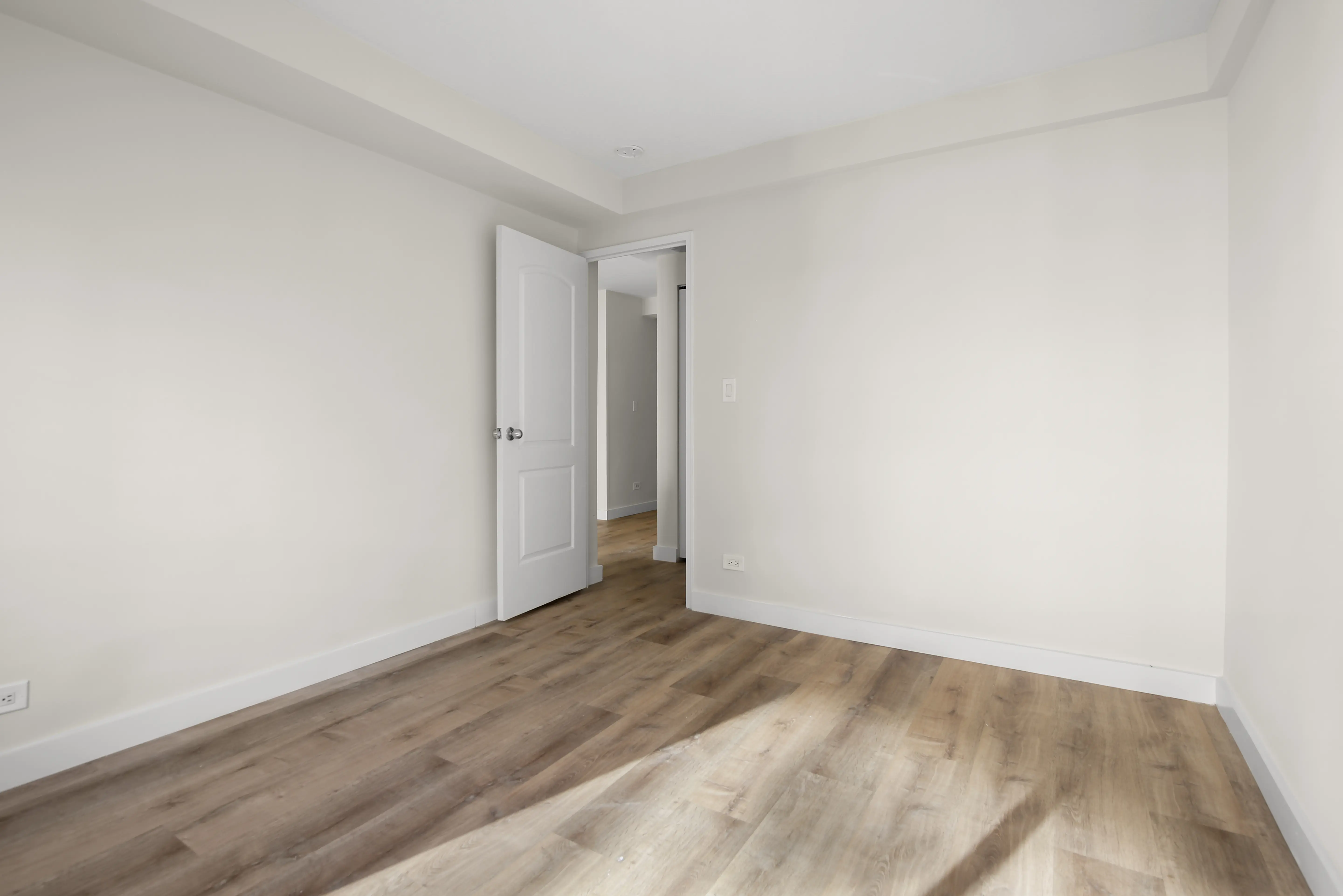 Empty room featuring wooden floors and white walls, creating a bright and spacious atmosphere.
