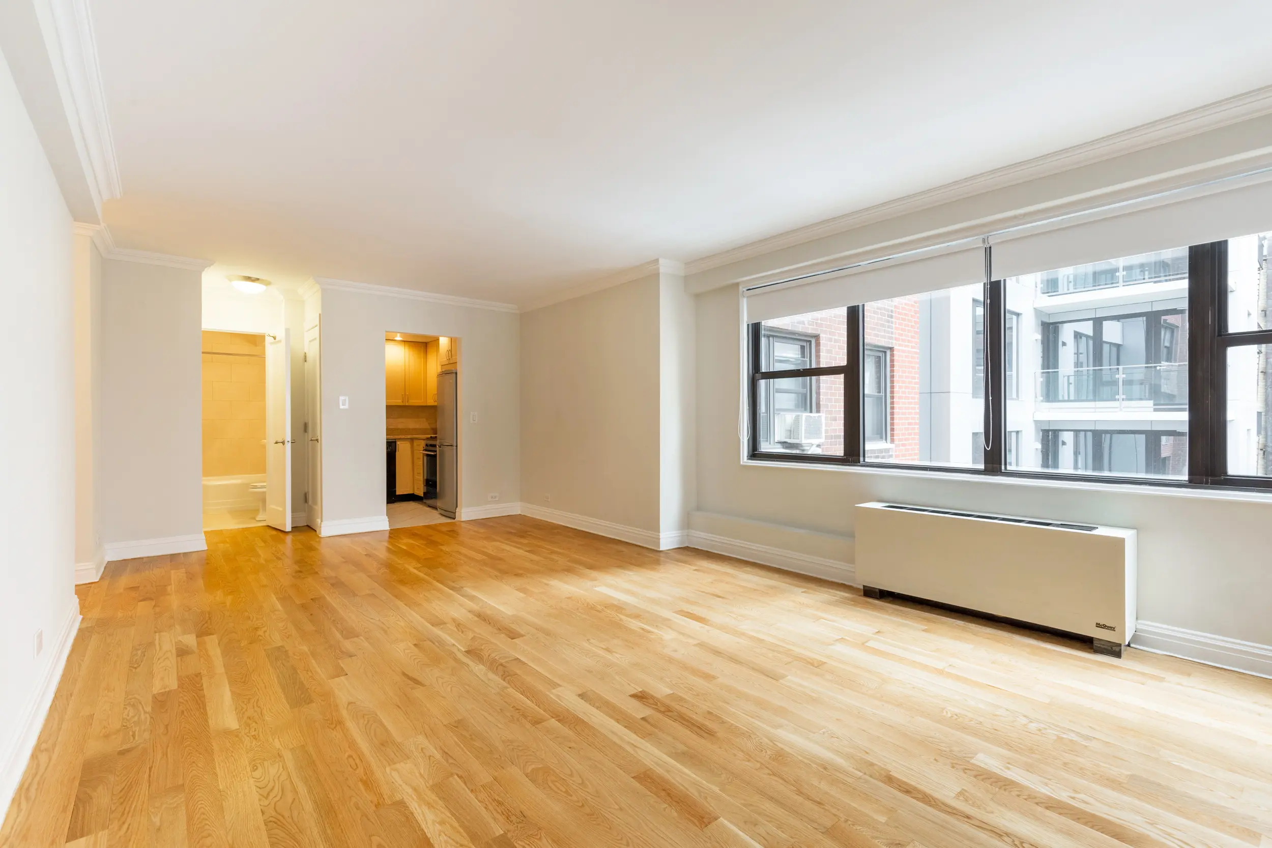 An empty apartment featuring hardwood floors and a large window allowing natural light to enter the space.