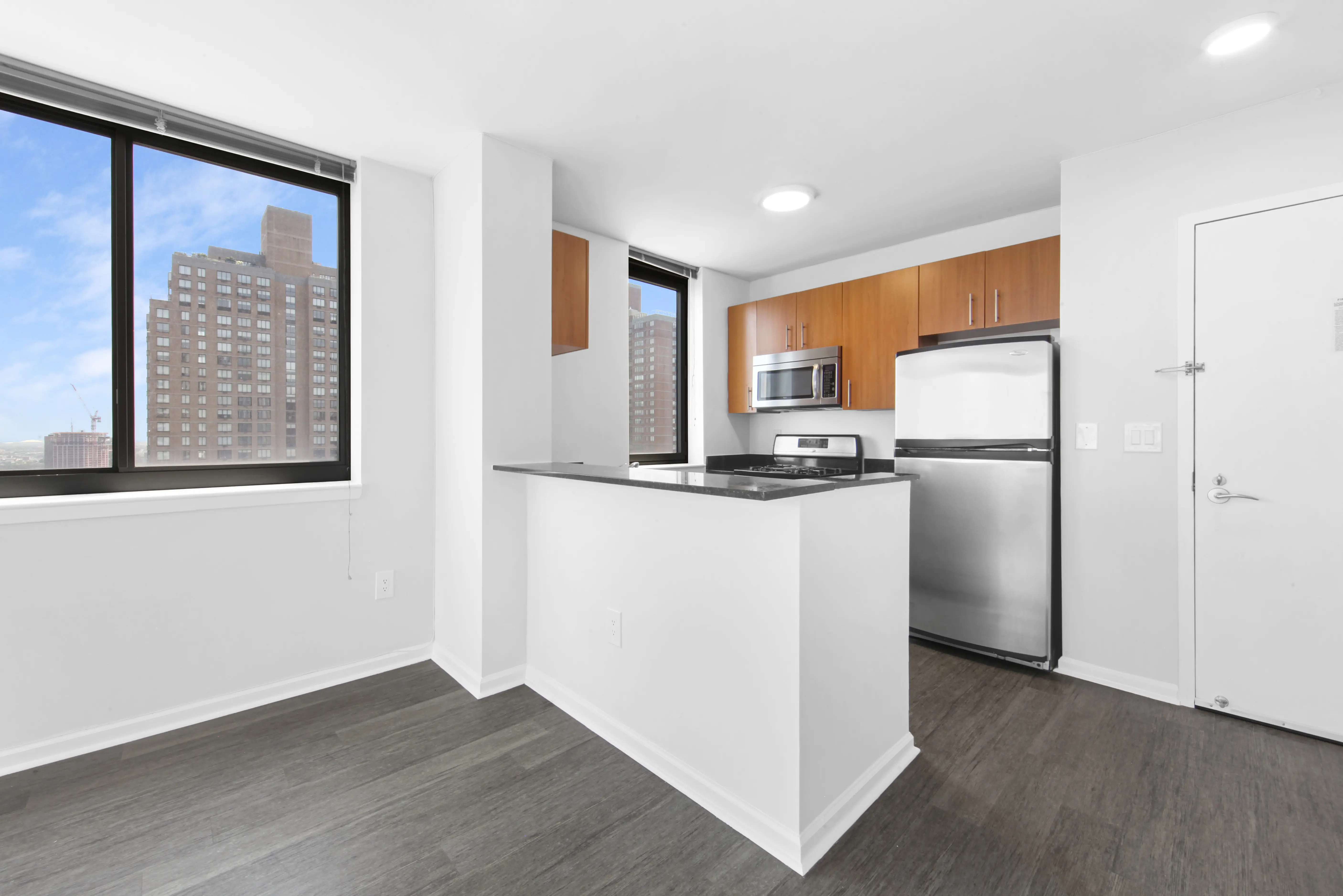 A modern kitchen showcasing a refrigerator, stove, and a window that brightens the room with sunlight.