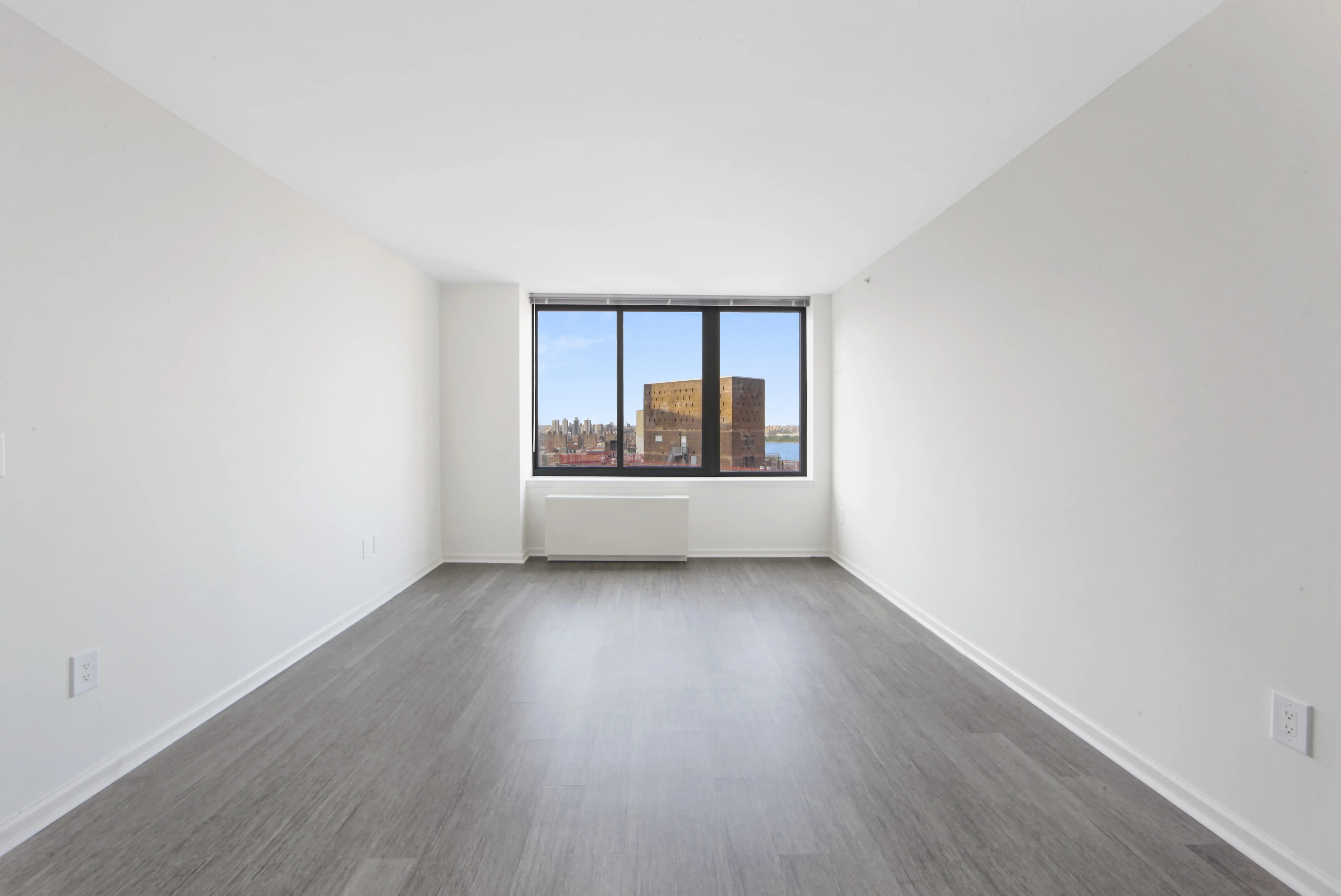 An empty apartment featuring hardwood floors and large windows allowing natural light to enter the space.