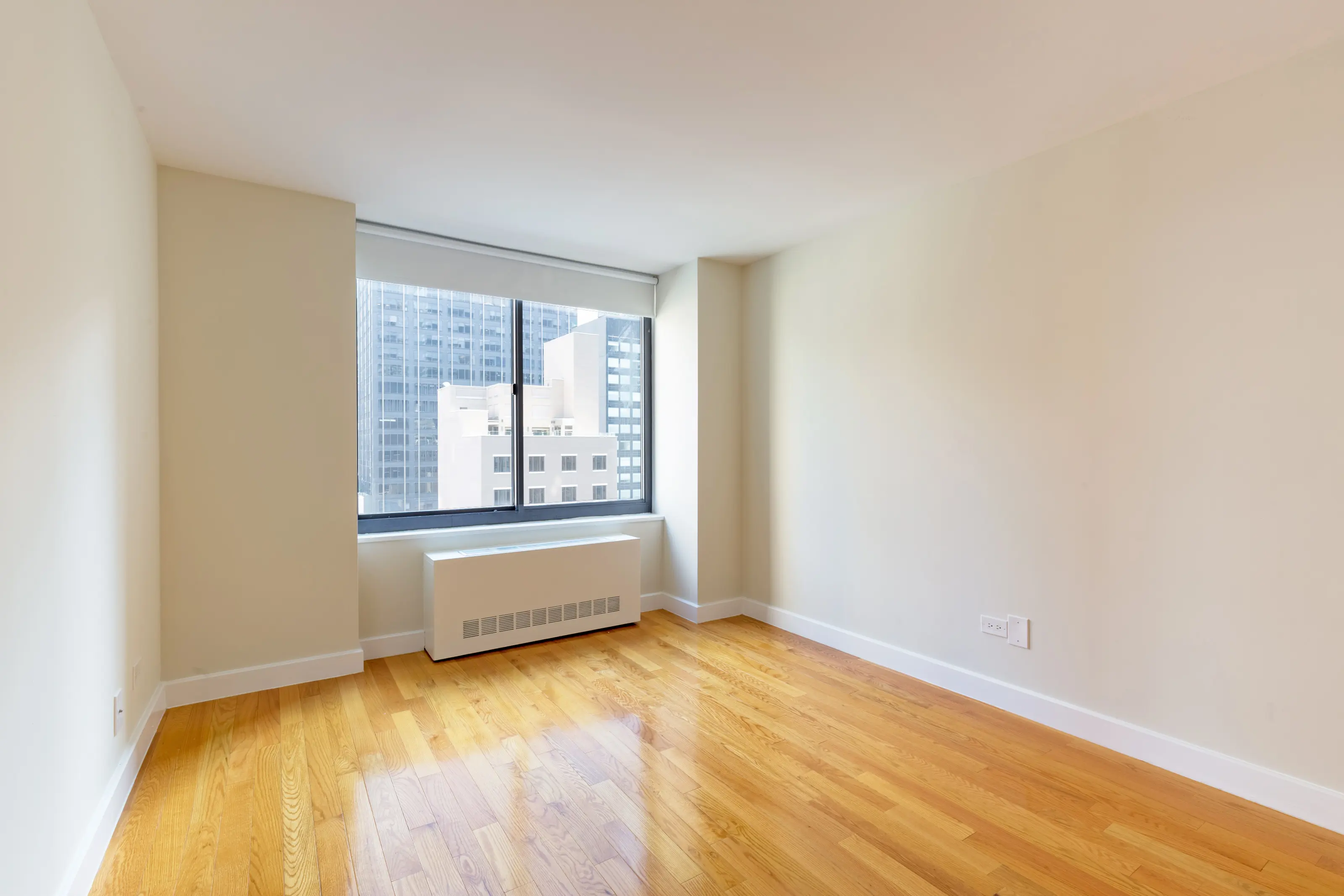 A vacant room with polished hardwood floors and a window, creating a bright and airy atmosphere.