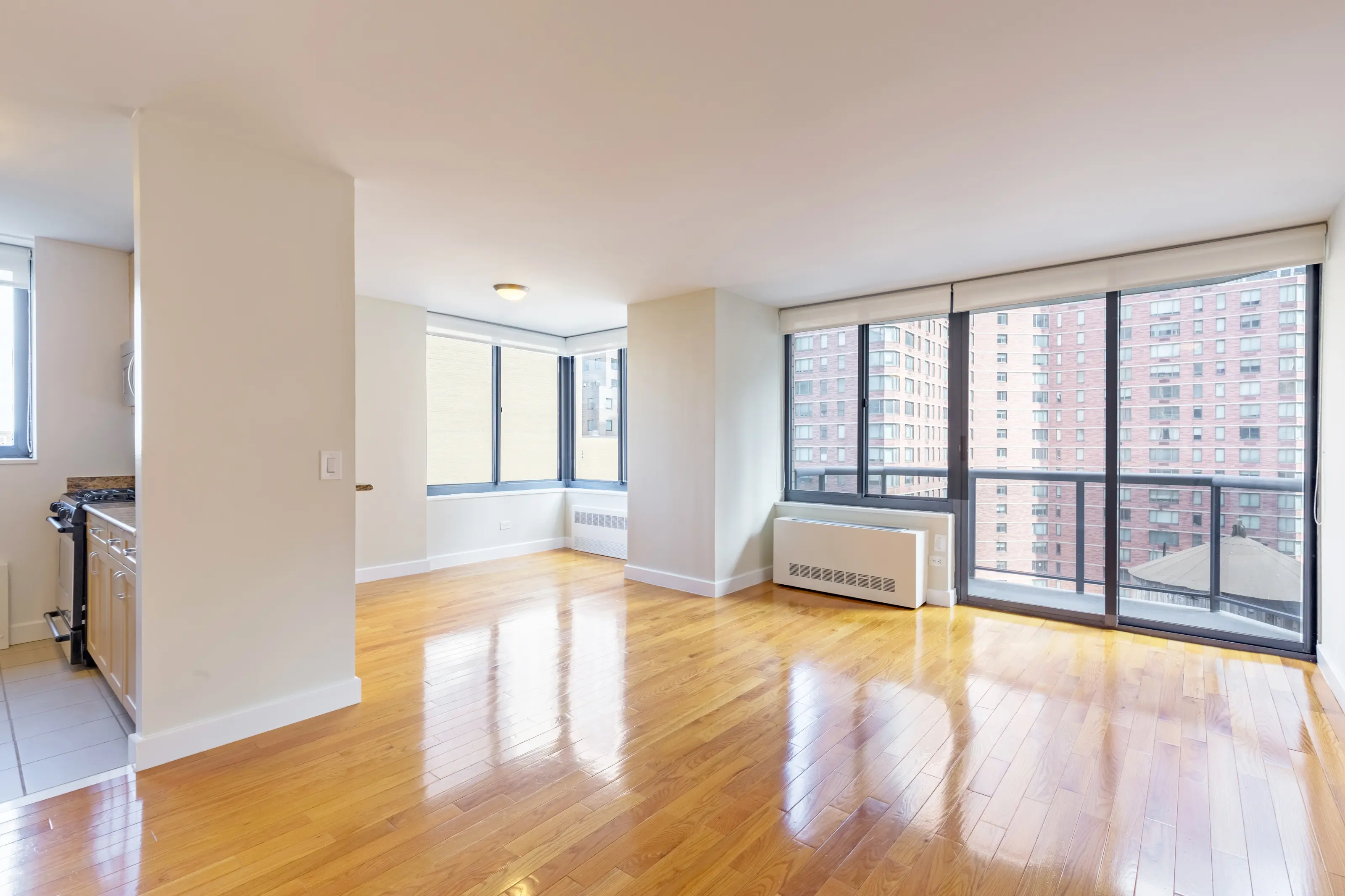 An unfurnished apartment with gleaming hardwood floors and expansive windows, providing a view of the outside.