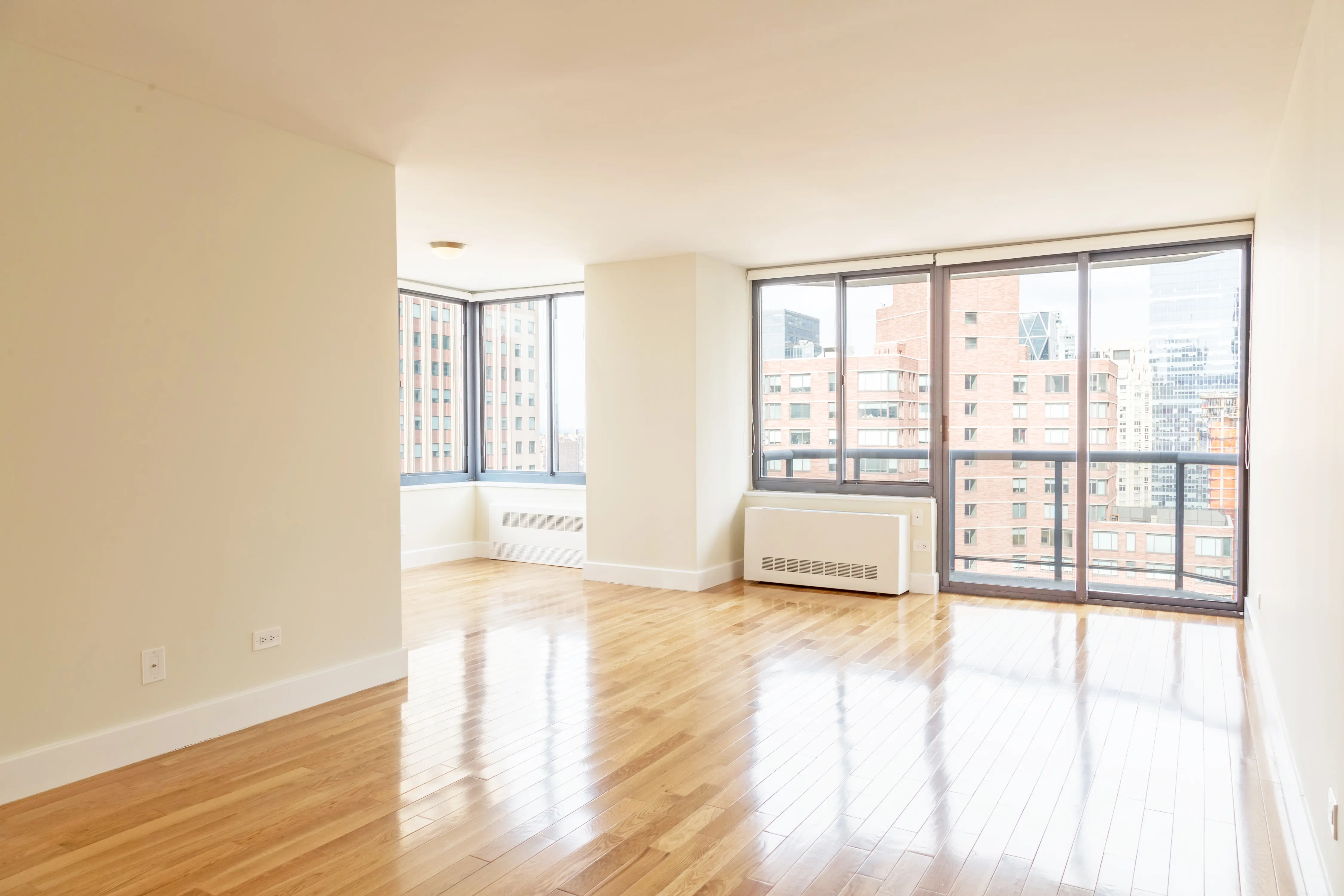 An empty apartment featuring hardwood floors and large windows, allowing ample natural light to fill the space.