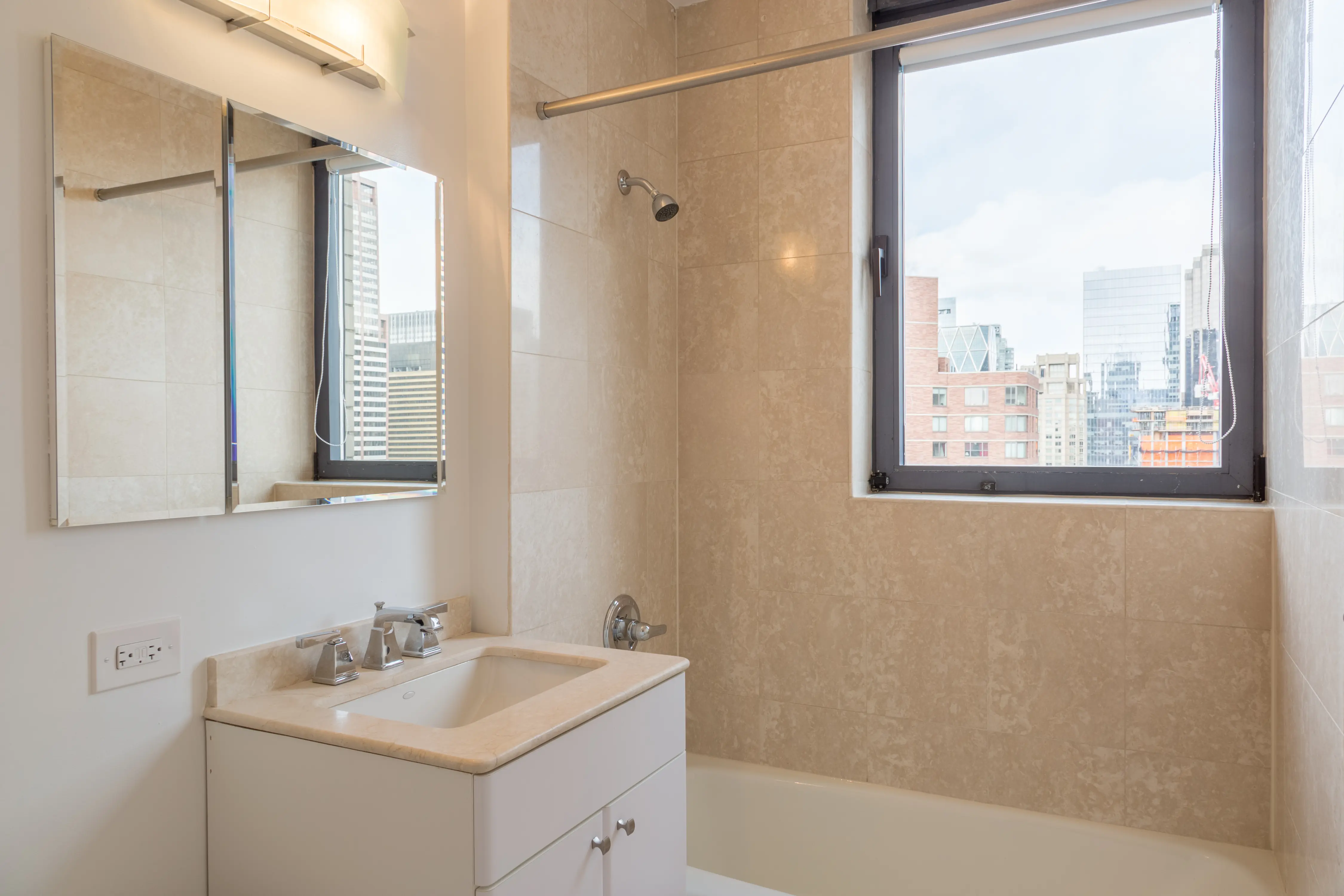 A clean bathroom with a sink, toilet, and a window offering a panoramic view of the city.
