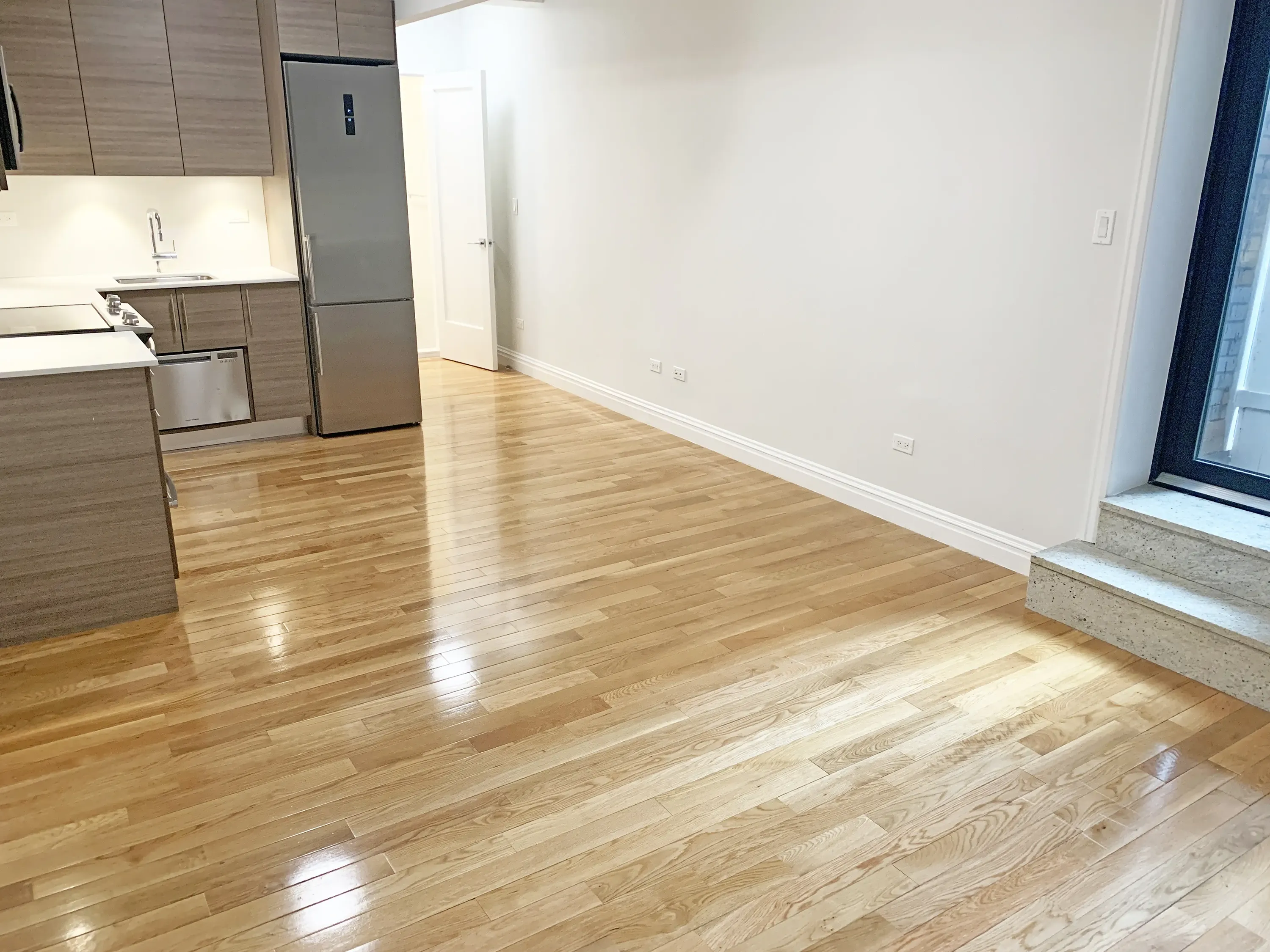 An empty apartment featuring hardwood floors and a modern kitchen, showcasing a spacious and minimalist design.