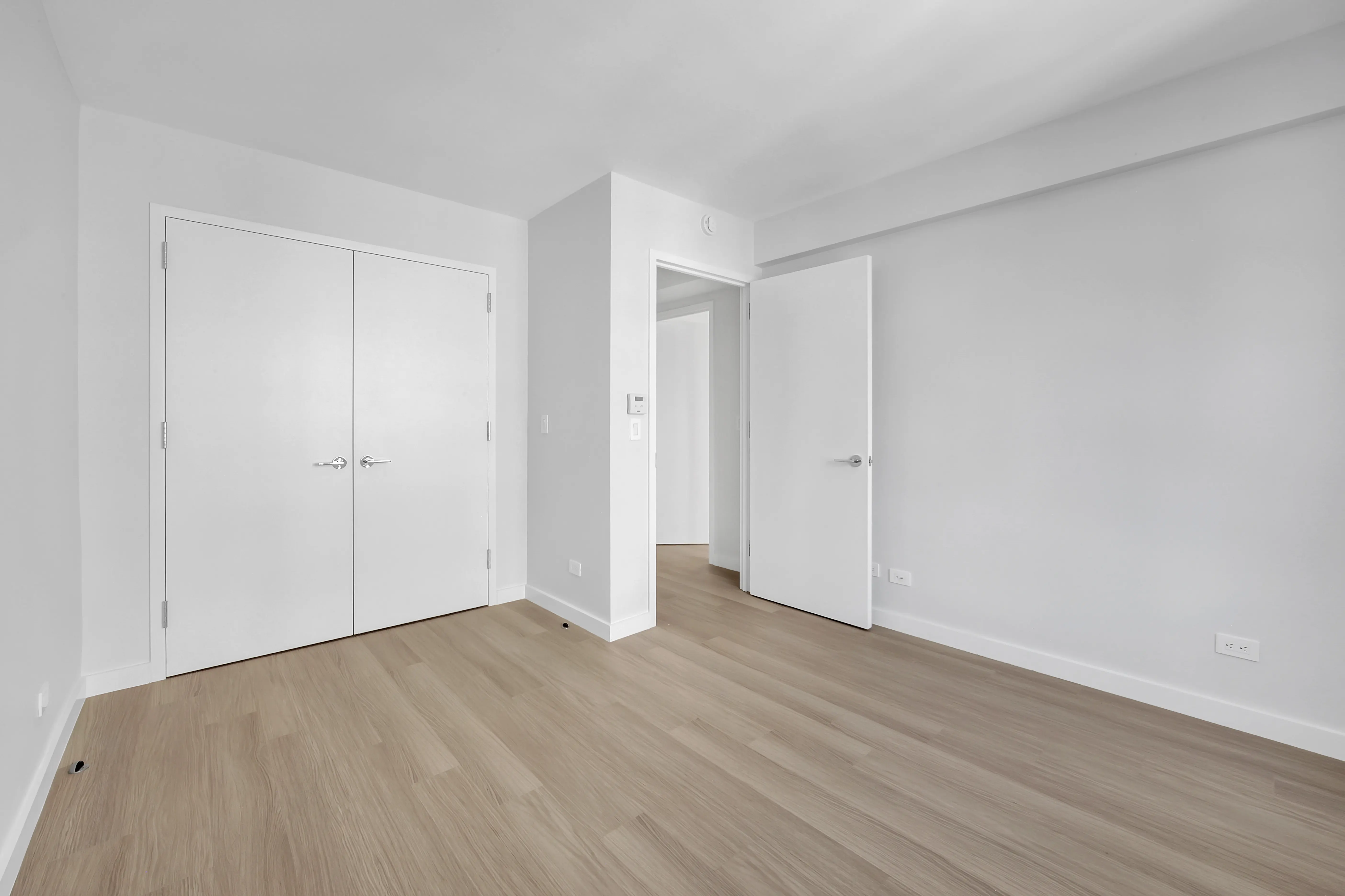 An unoccupied room showcasing white walls and natural wooden floors, offering a clean and minimalist aesthetic.