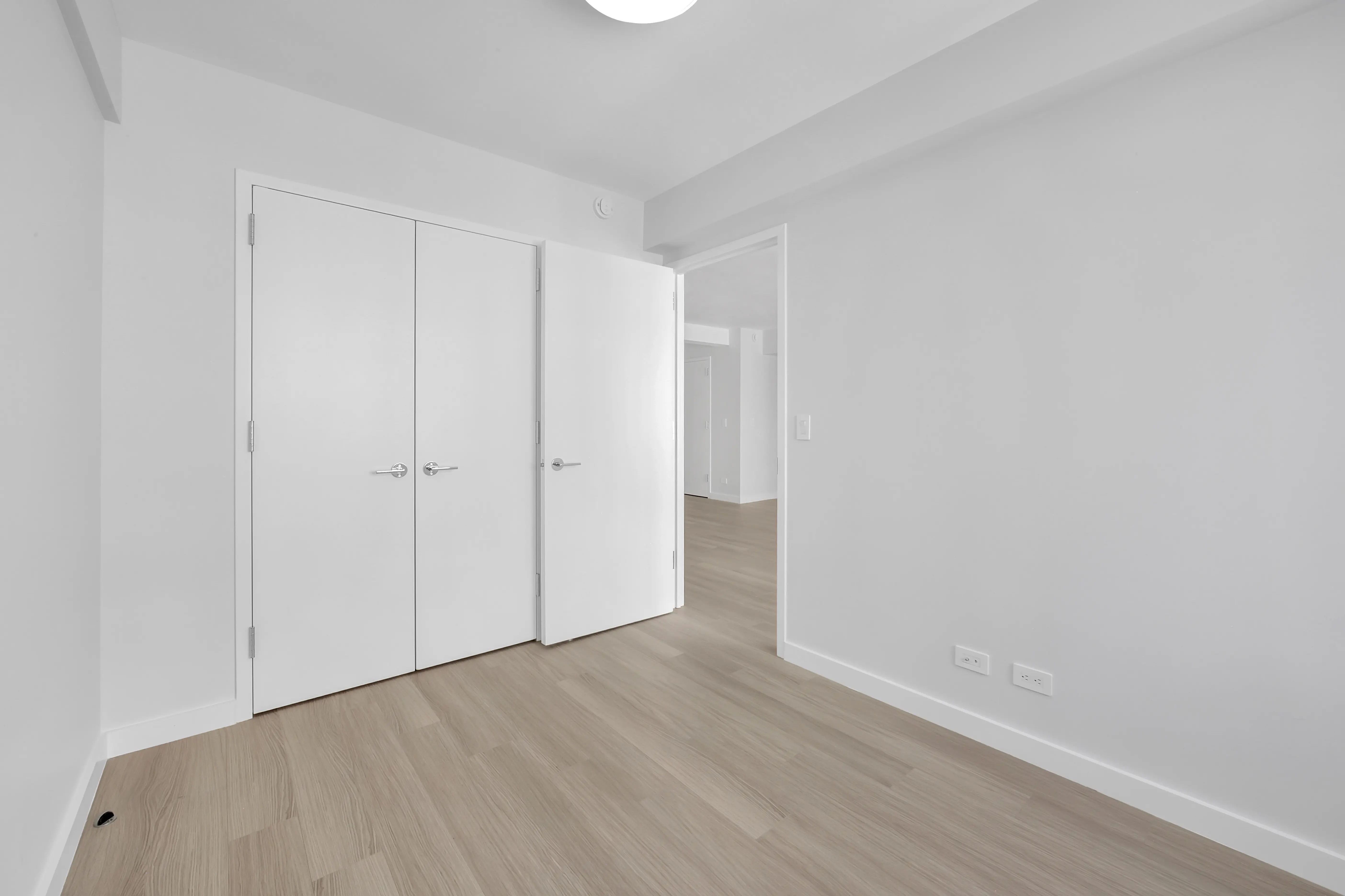 A bright white room featuring wooden floors and white doors, creating a clean and minimalist aesthetic.