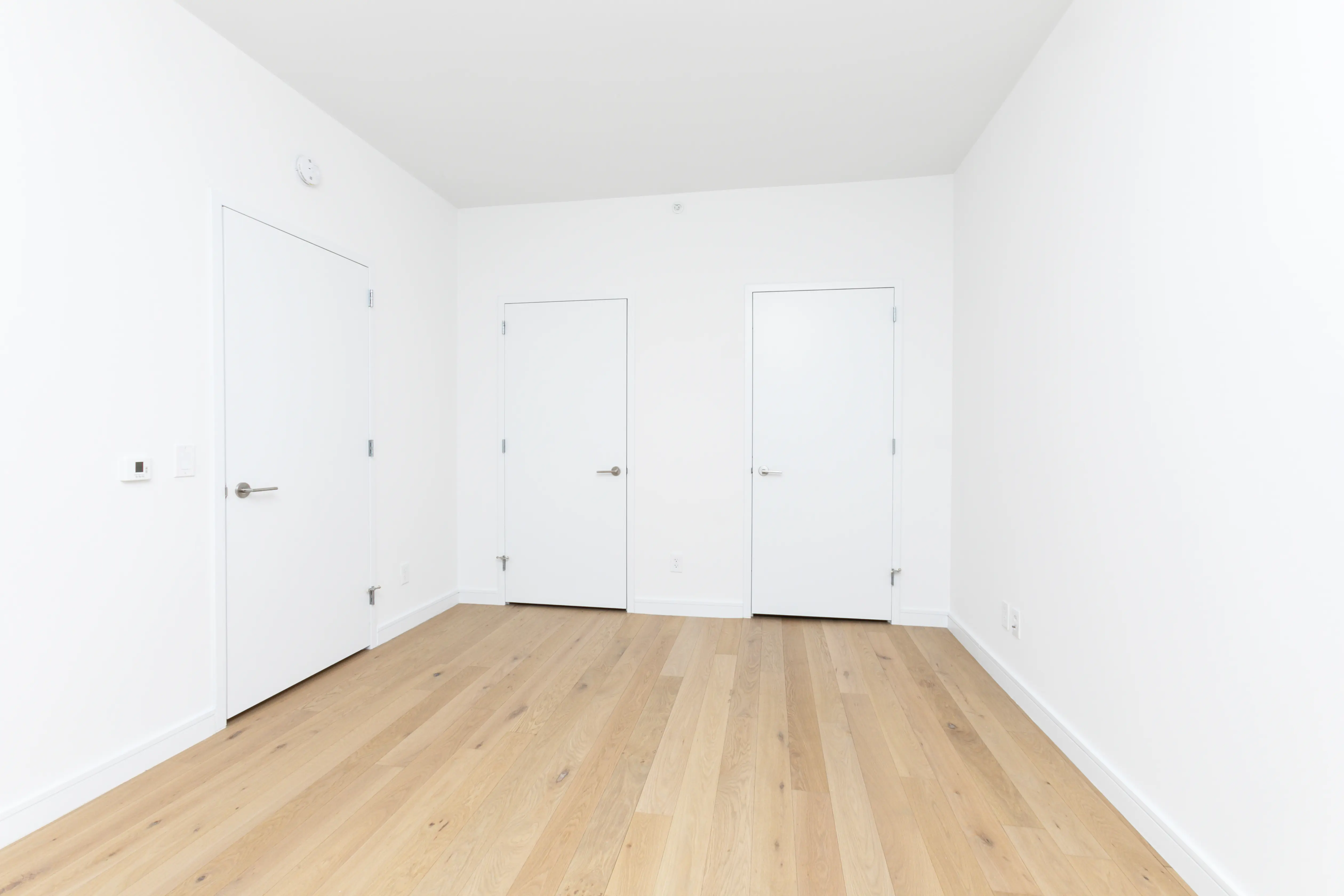 A bright white room featuring two doors and polished hardwood floors.