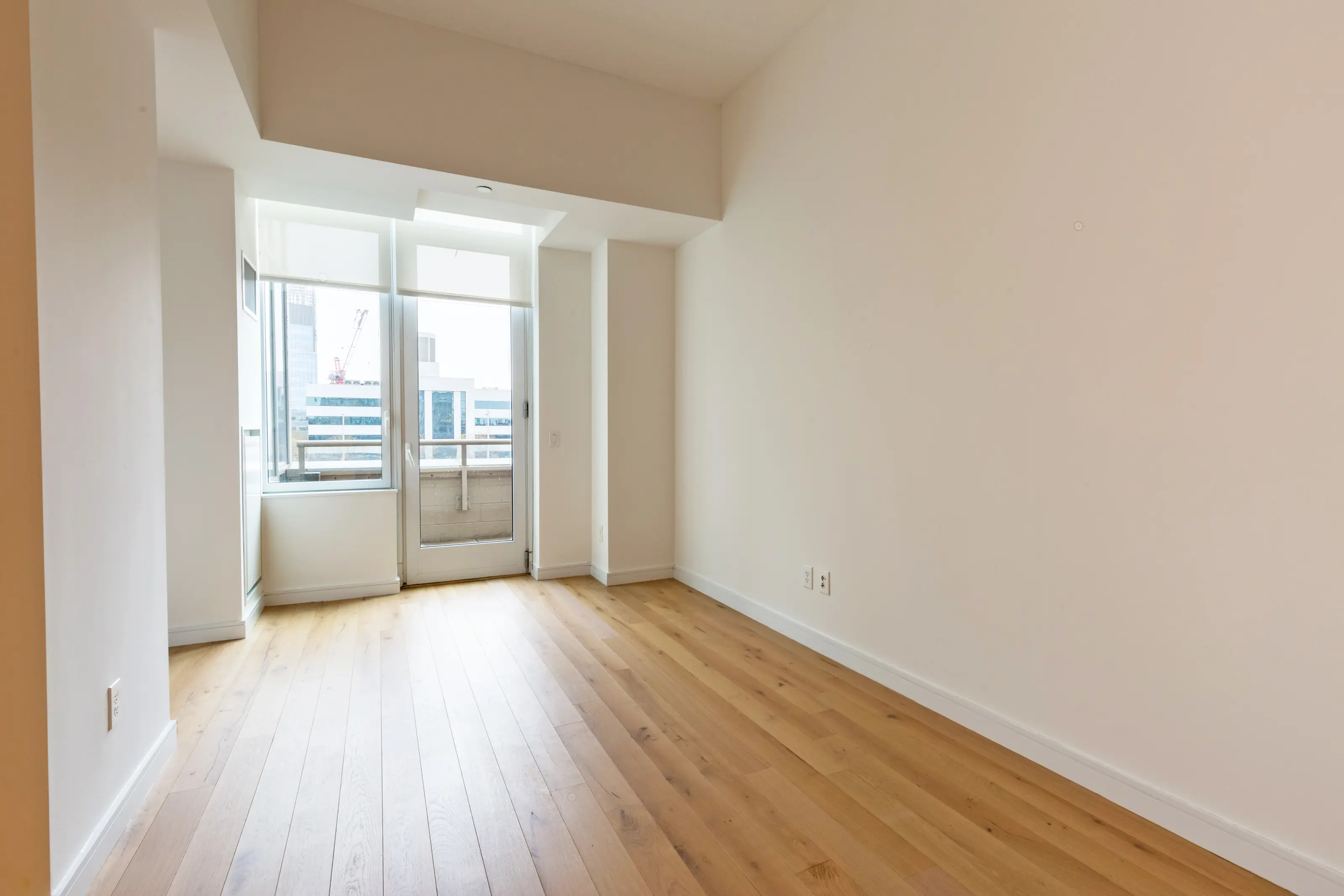 An empty room featuring hardwood floors and a large window allowing natural light to enter.